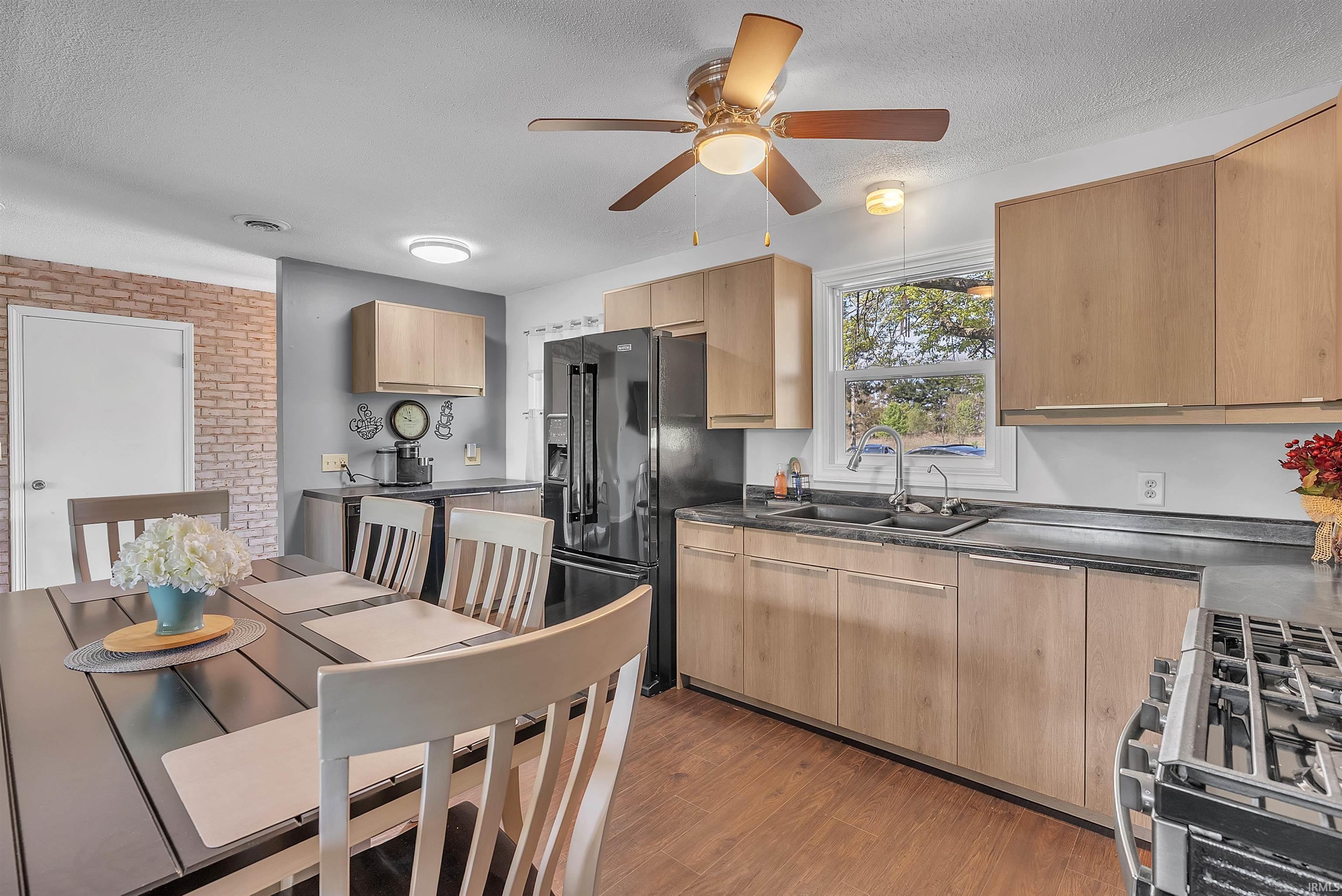 Image 2: Kitchen area featuring wood-finish flooring, light wood-look cabinetry, dark countertops, and a black refrigerator, Kitchen