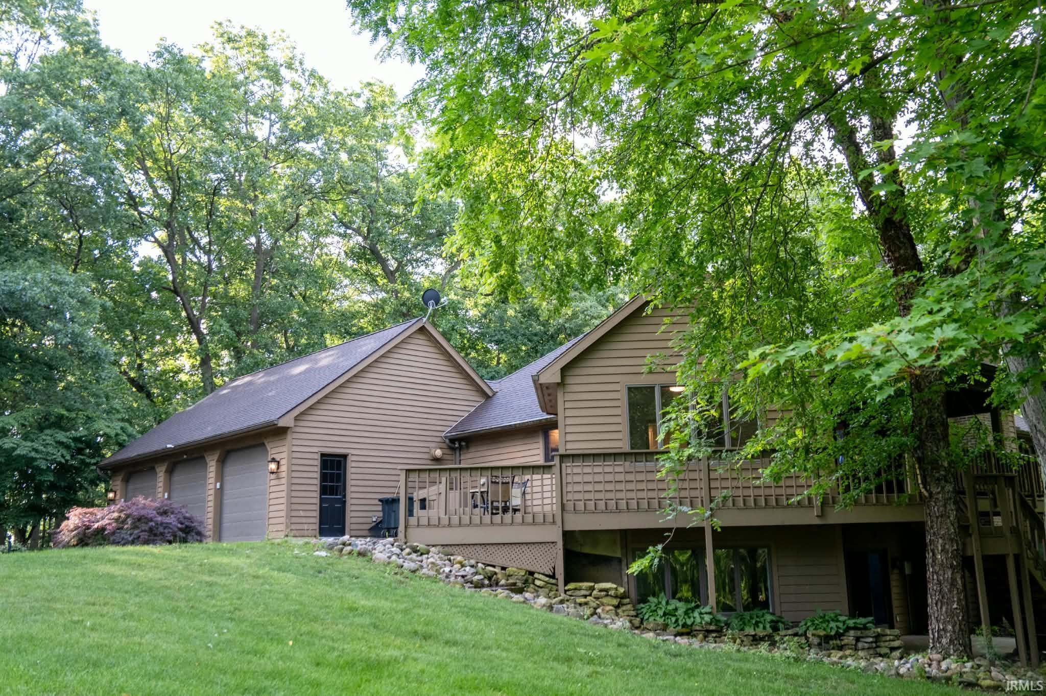 Image 3: Multi-level residence featuring a three-car garage with individual doors, a spacious wood-finish deck with privacy lattice, and a lower-level walk-out, Back Of Structure Image 3: Multi-level residence featuring a three-car garage with individual doors, a spacious wood-finish deck with privacy lattice, and a lower-level walk-out, Back Of Structure