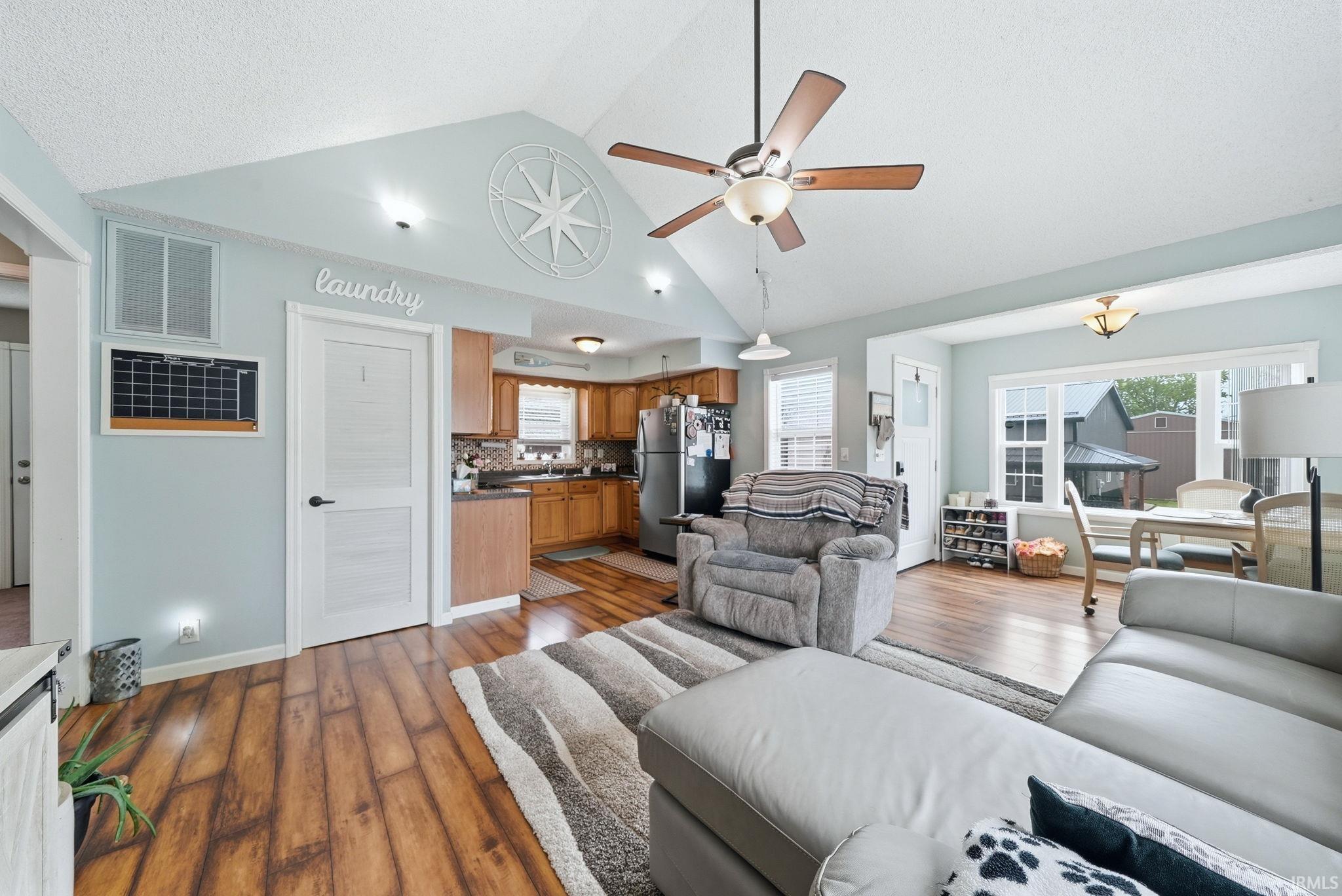Image 2: Open-concept living area featuring vaulted ceilings, wood-finish flooring, a ceiling fan, recessed lighting, and a kitchen with wood cabinetry and stainless steel appliances, Living Room Image 2: Open-concept living area featuring vaulted ceilings, wood-finish flooring, a ceiling fan, recessed lighting, and a kitchen with wood cabinetry and stainless steel appliances, Living Room