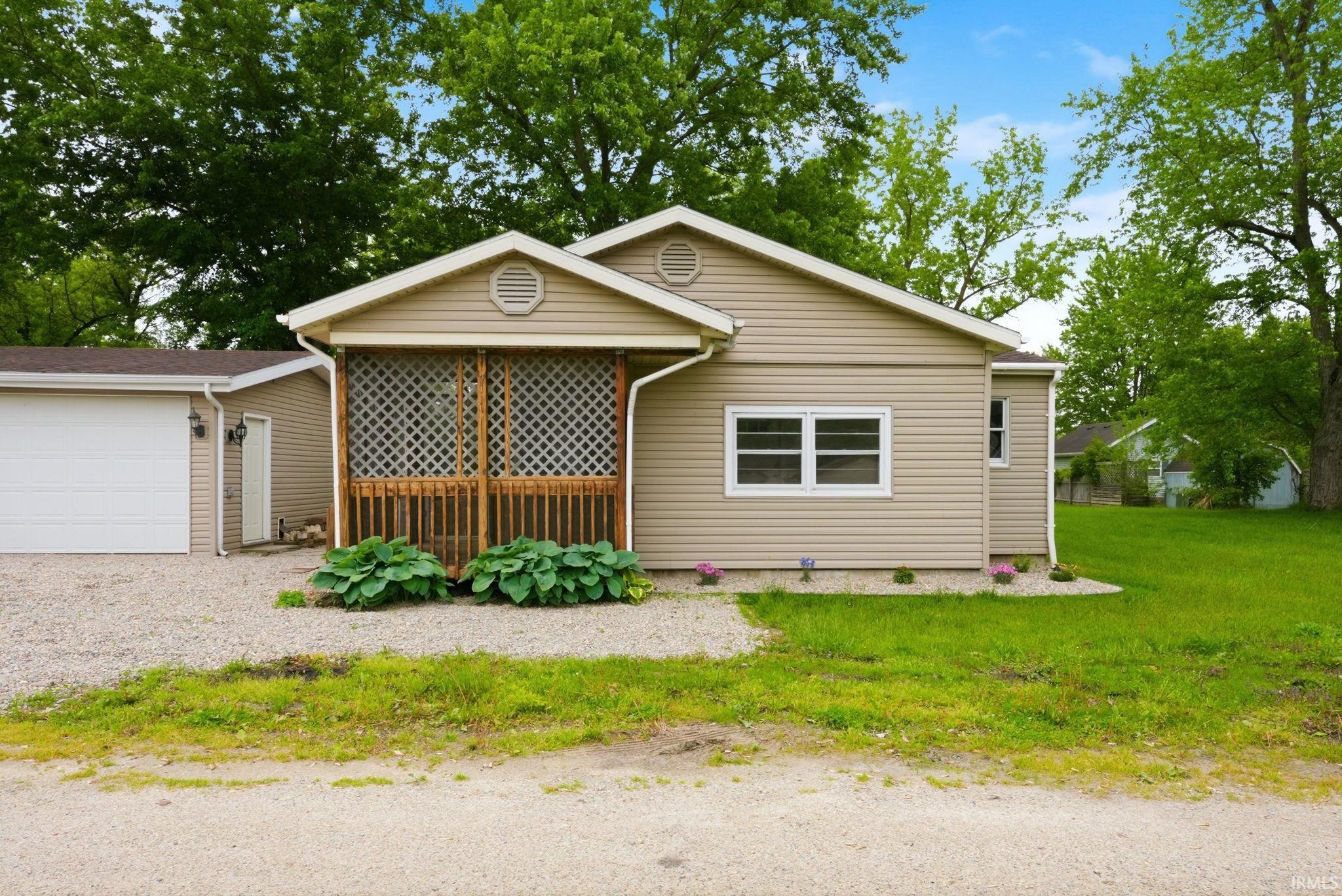 Image 1: Single-story residence featuring tan horizontal siding, a screened porch with wood-finish railing and lattice, a white garage door, and white frame windows, Front Of Structure