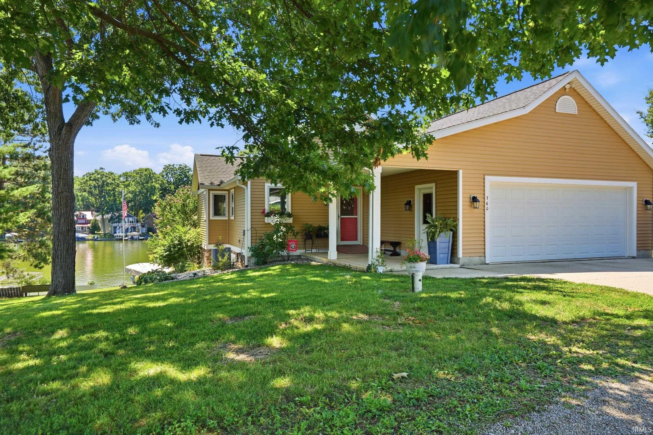 Image 3: Waterfront property featuring a two-car garage, covered porch entry, and a mature tree providing shade, Front Of Structure Image 3: Waterfront property featuring a two-car garage, covered porch entry, and a mature tree providing shade, Front Of Structure
