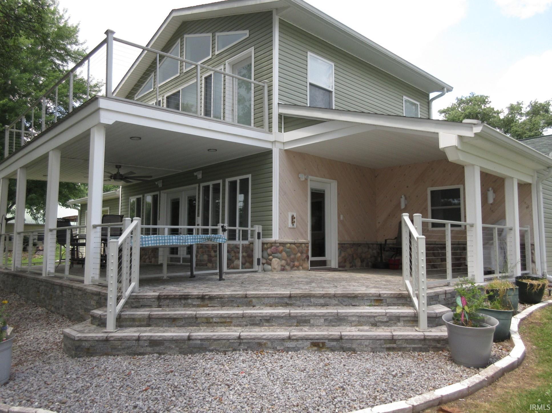 Image 1: Multi-level outdoor living space featuring a covered patio, upper balcony with glass railing, and stone-clad exterior accents, Lake Front and Side