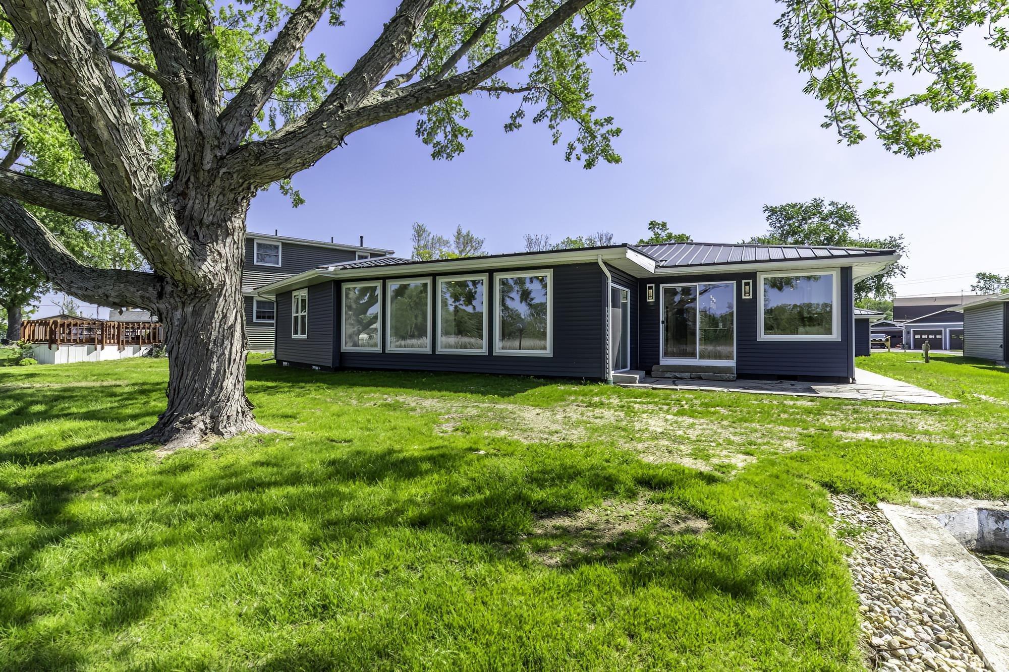 Image 1: Contemporary siding exterior with a metal roof, expansive windows, a sliding glass door, an outdoor patio area, and a large mature tree, Back Of Structure Image 1: Contemporary siding exterior with a metal roof, expansive windows, a sliding glass door, an outdoor patio area, and a large mature tree, Back Of Structure
