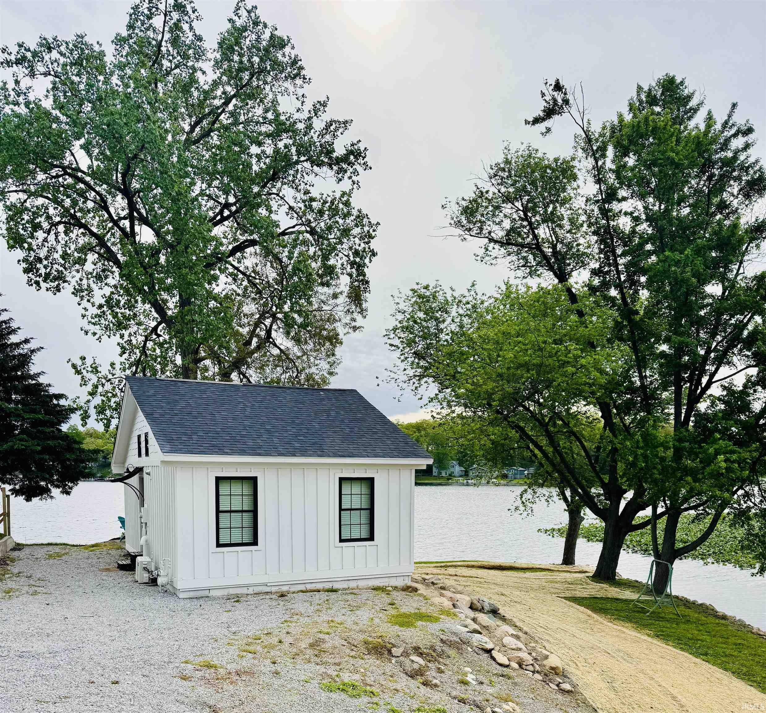 Image 3: White board-and-batten structure with black-trimmed windows, a dark shingle roof, and a gravel surround, Out Buildings Image 3: White board-and-batten structure with black-trimmed windows, a dark shingle roof, and a gravel surround, Out Buildings