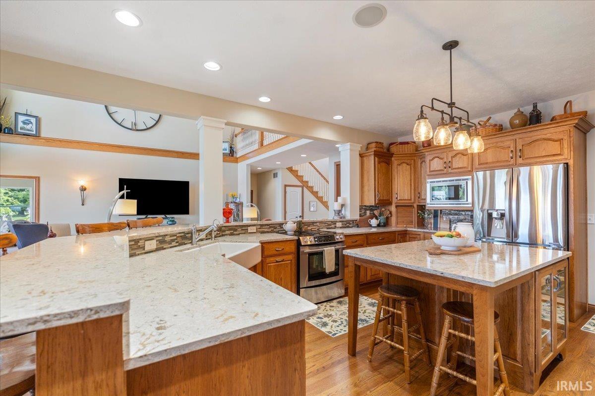 Image 1: Open-concept island kitchen featuring light-toned quartz countertops, wood cabinetry, stainless steel appliances, and a central island with built in storage and seating, Island Kitchen Image 1: Open-concept island kitchen featuring light-toned quartz countertops, wood cabinetry, stainless steel appliances, and a central island with built in storage and seating, Island Kitchen