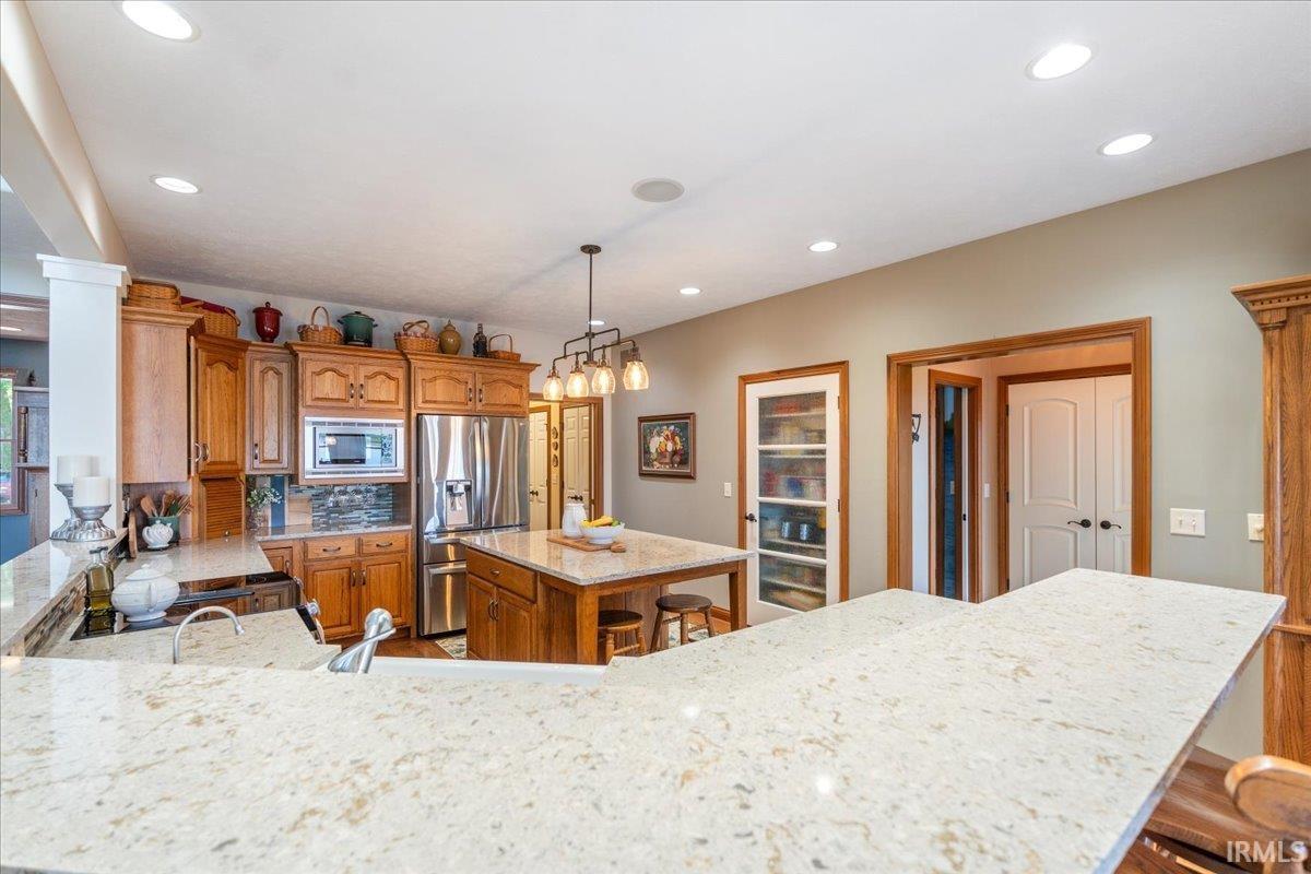 Image 3: Kitchen featuring light-toned countertops, wood cabinetry, stainless steel appliances, a central island with seating, and recessed lighting, Island Kitchen Image 3: Kitchen featuring light-toned countertops, wood cabinetry, stainless steel appliances, a central island with seating, and recessed lighting, Island Kitchen