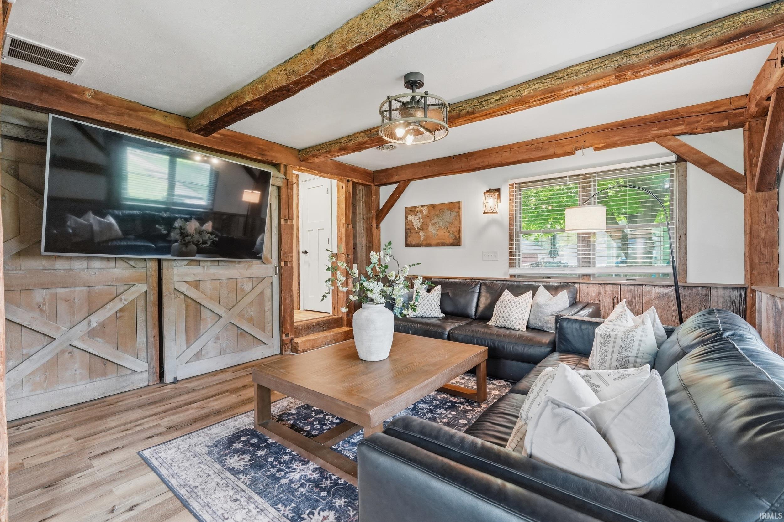 Image 2: Living area featuring exposed wood beams, wood-finish flooring, and a large window with blinds, Living Room Image 2: Living area featuring exposed wood beams, wood-finish flooring, and a large window with blinds, Living Room
