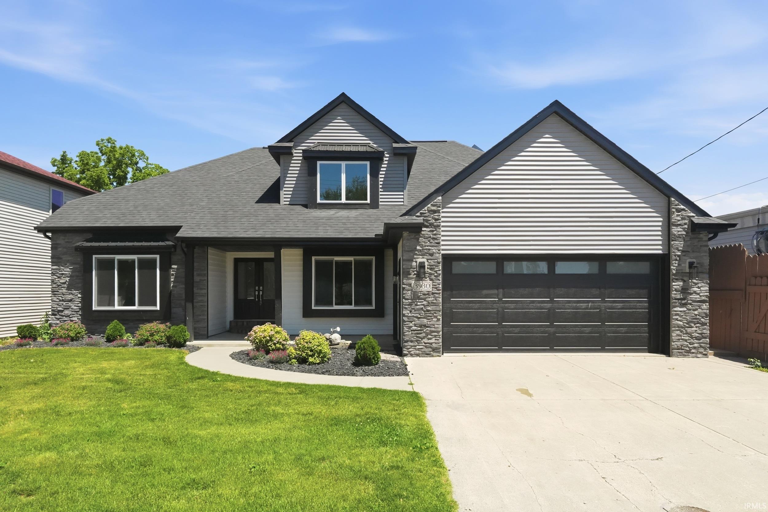 Image 0: Contemporary home featuring a dark shingle roof, stone veneer accents, light horizontal siding, a two-car garage with frosted window panels, and a concrete driveway, Front Of Structure Image 0: Contemporary home featuring a dark shingle roof, stone veneer accents, light horizontal siding, a two-car garage with frosted window panels, and a concrete driveway, Front Of Structure
