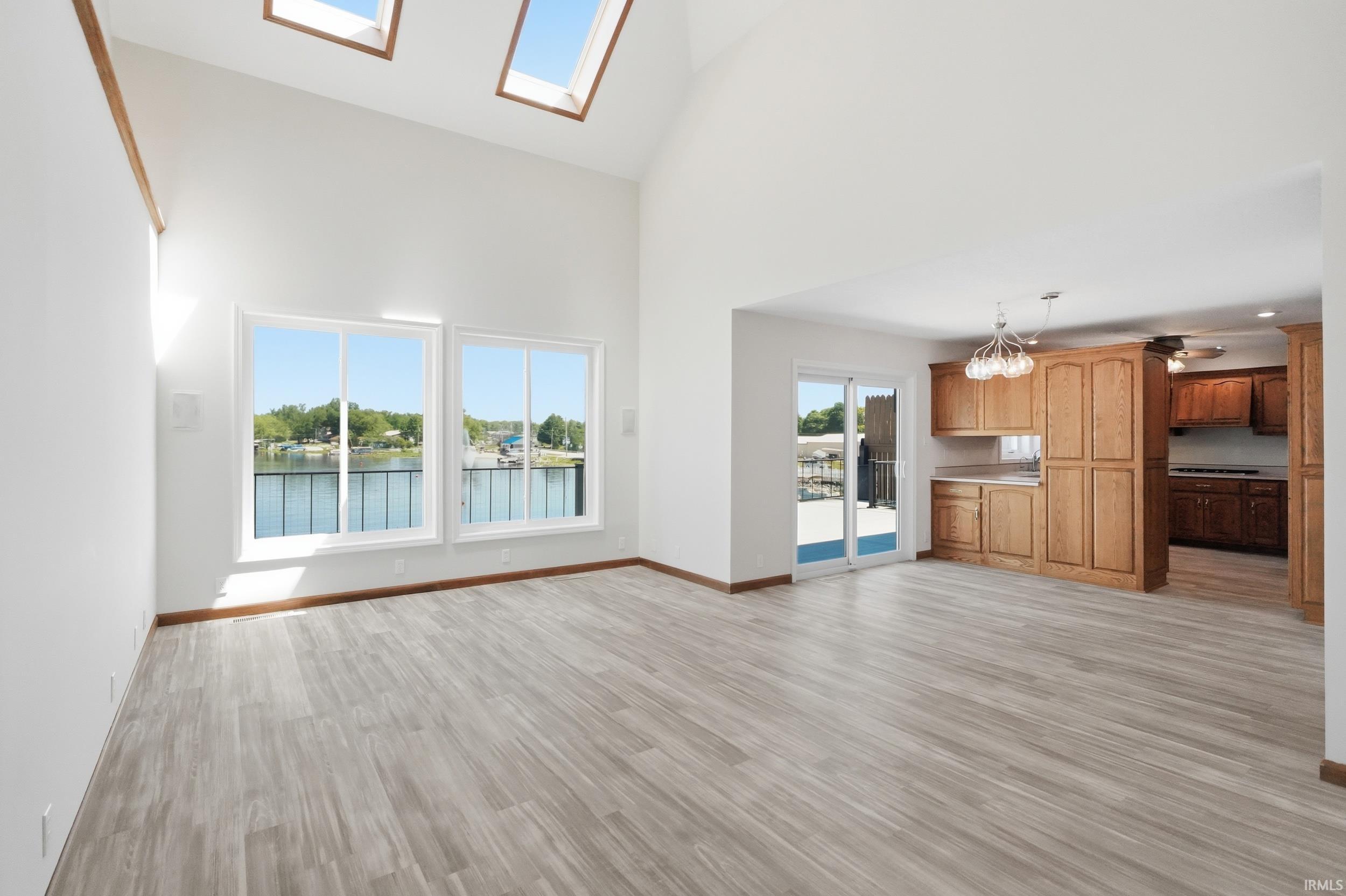 Image 3: Vaulted ceiling great room featuring wood-finish flooring, multiple skylights, and large windows with water scenery, Living Room Image 3: Vaulted ceiling great room featuring wood-finish flooring, multiple skylights, and large windows with water scenery, Living Room
