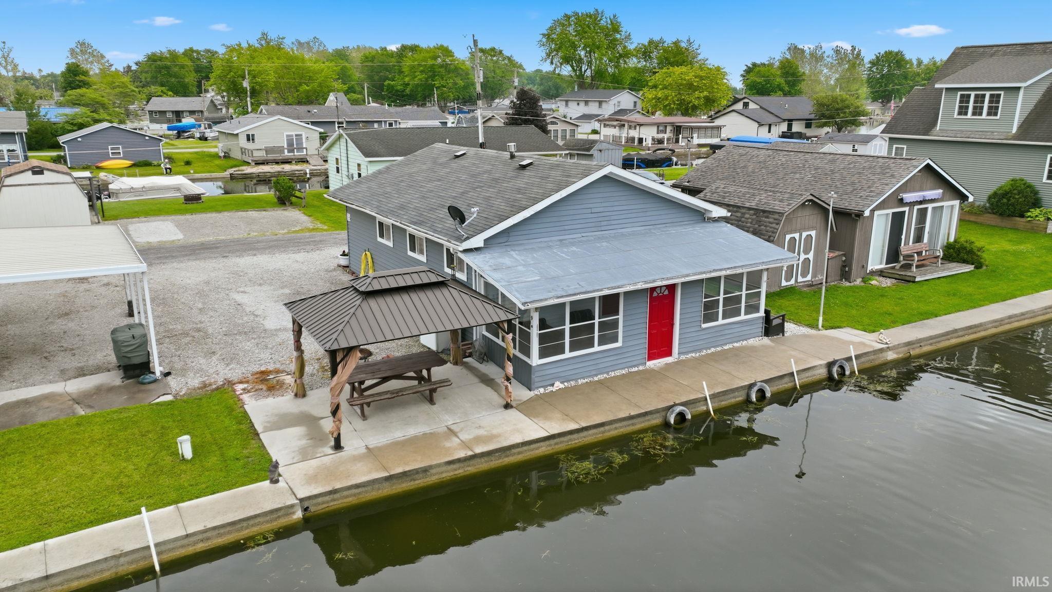 Image 1: Waterfront property featuring a blue siding exterior with a contrasting red entry door, Back Of Structure