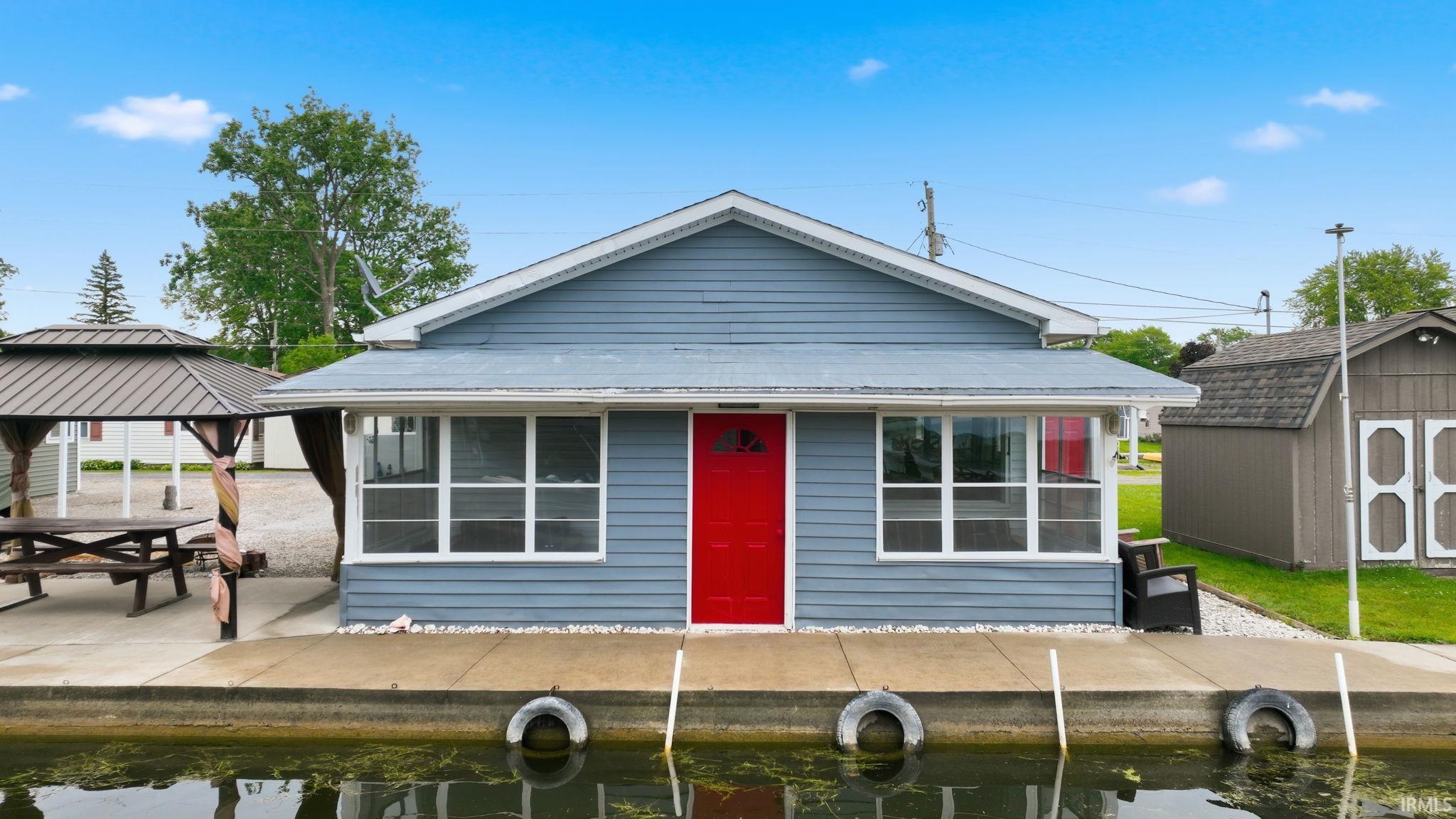 Image 3: Waterfront cottage featuring light blue siding, a vibrant red entry door, and white-framed windows, Front Of Structure