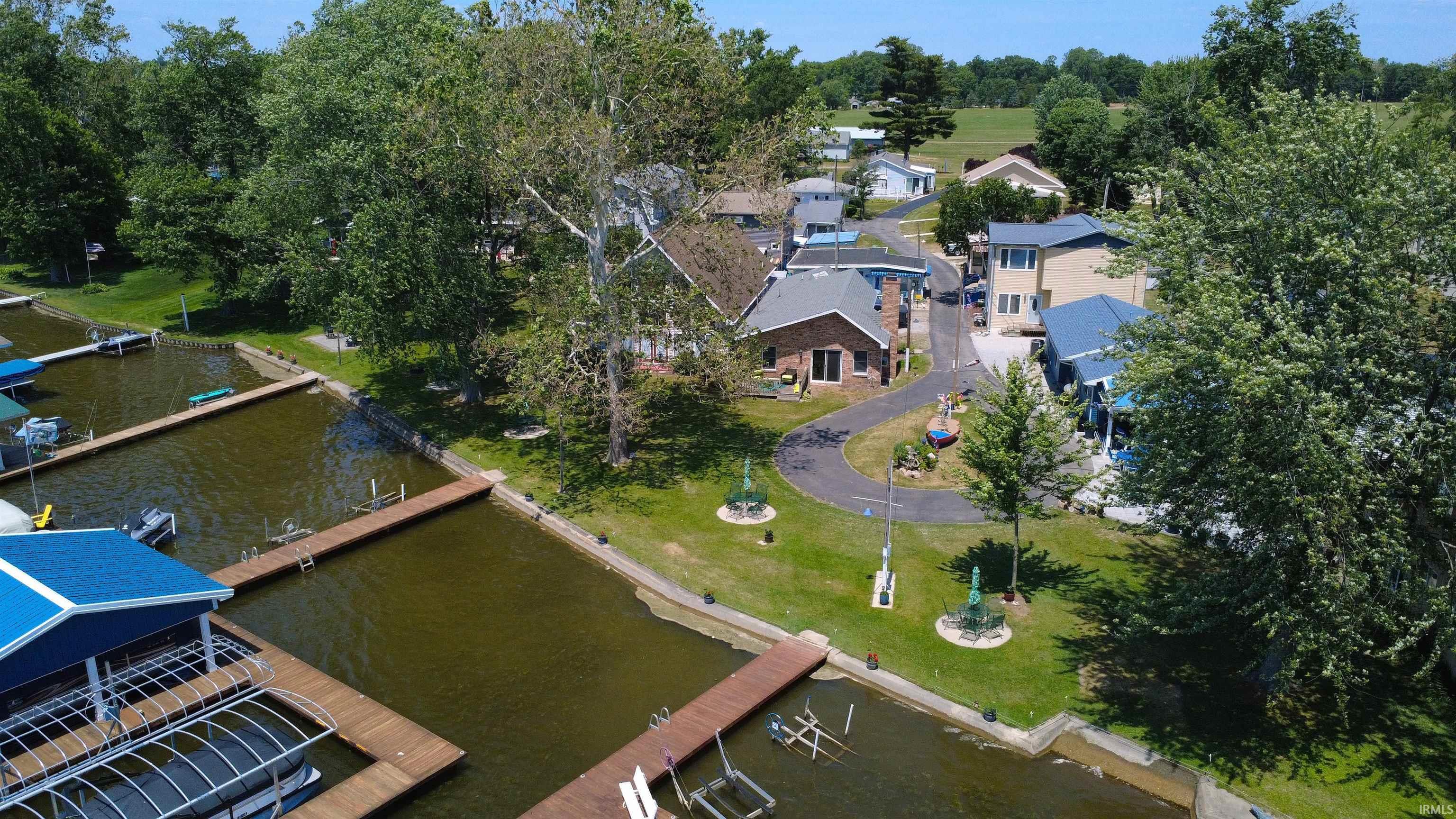 Image 0: Waterfront property featuring private boat docks, a manicured lawn, paved driveway, mature trees, and a brick exterior, Aerial View Image 0: Waterfront property featuring private boat docks, a manicured lawn, paved driveway, mature trees, and a brick exterior, Aerial View