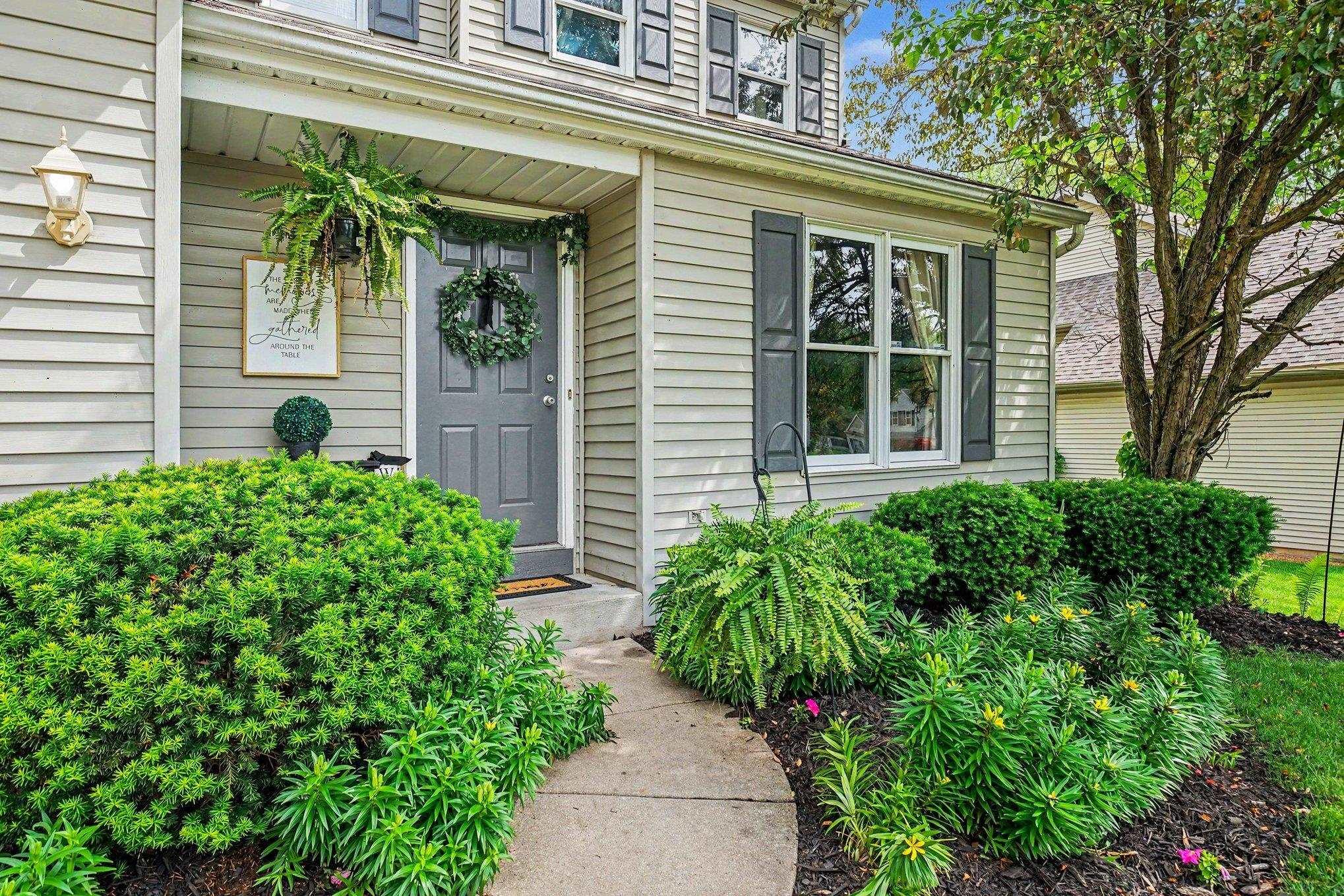 Image 2: Cream-colored siding exterior featuring a gray paneled front door, dark gray window shutters, an exterior wall light fixture, and a concrete pathway, Entry
