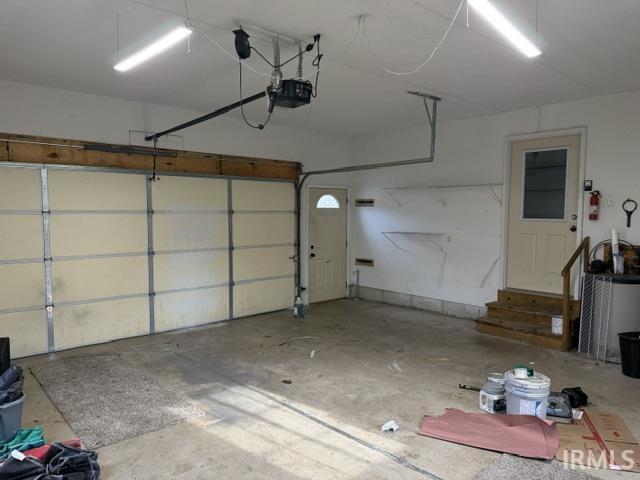 Image 1: Garage interior featuring a sectional garage door with automatic opener, two fluorescent light fixtures, concrete flooring, and a side entry door with steps, Garage Image 1: Garage interior featuring a sectional garage door with automatic opener, two fluorescent light fixtures, concrete flooring, and a side entry door with steps, Garage