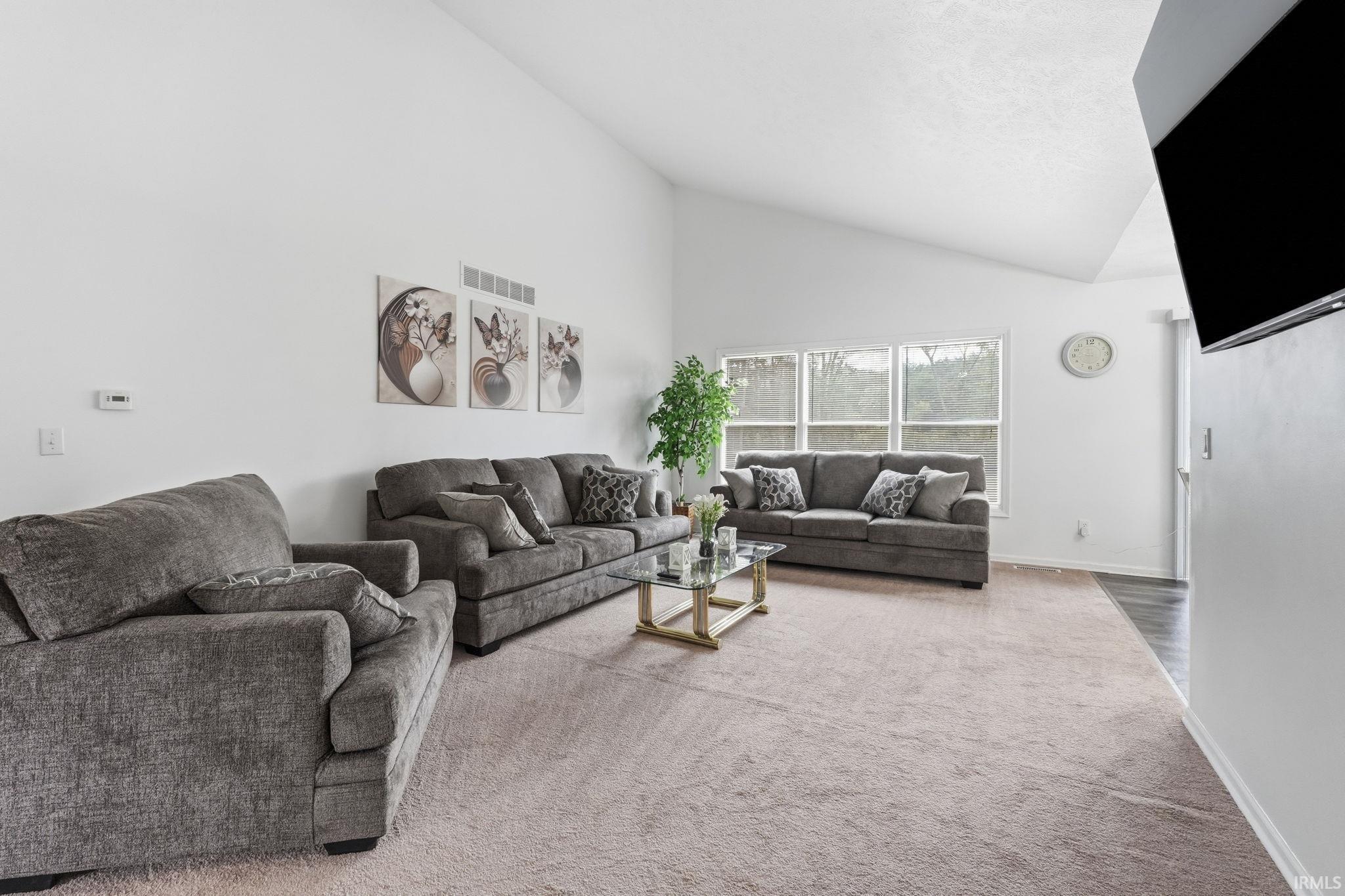 Image 1: Vaulted ceiling, multiple windows, light-toned carpeting, and a wall-mounted television, Living Room Image 1: Vaulted ceiling, multiple windows, light-toned carpeting, and a wall-mounted television, Living Room