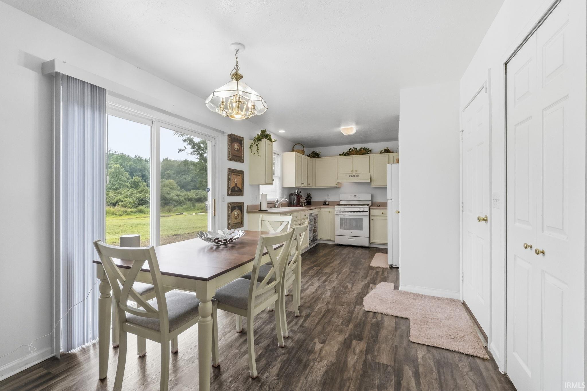 Image 2: Kitchen and dining area featuring wood-finish flooring, sliding glass door, overhead chandelier, paneled cabinetry, and a range oven, Dining Area Image 2: Kitchen and dining area featuring wood-finish flooring, sliding glass door, overhead chandelier, paneled cabinetry, and a range oven, Dining Area
