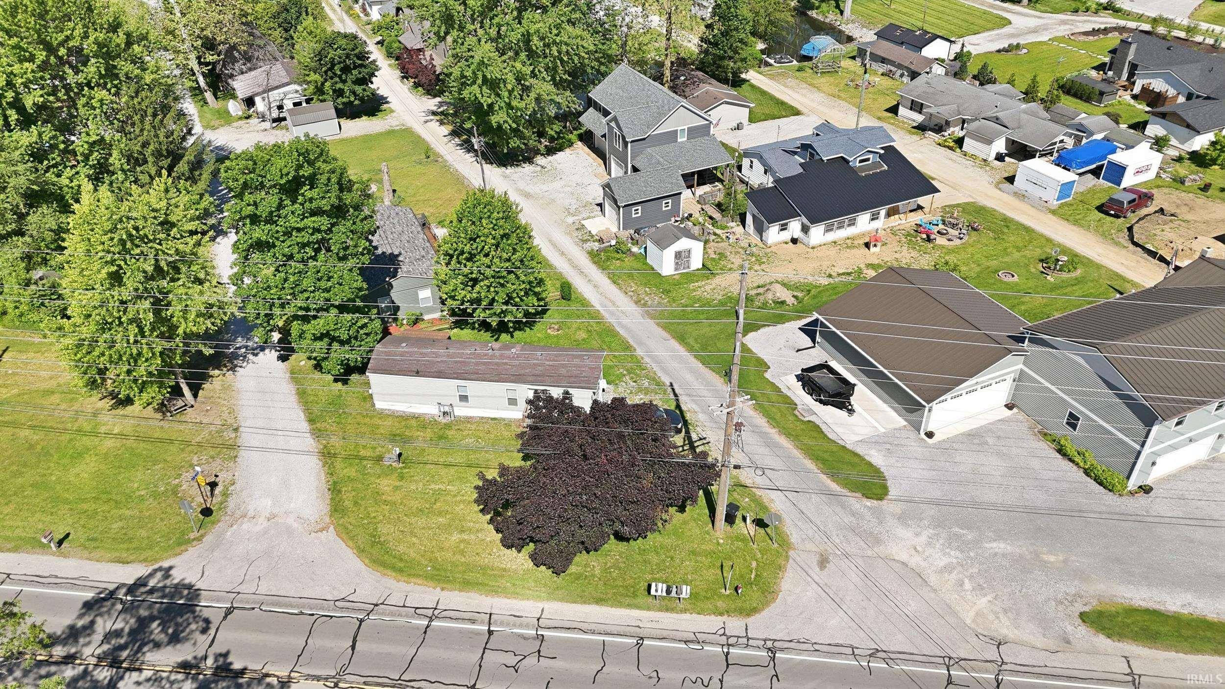 Image 2: Aerial perspective showcasing a property with a gravel driveway, mature trees, and a light-colored structure with a brown roof, Aerial View