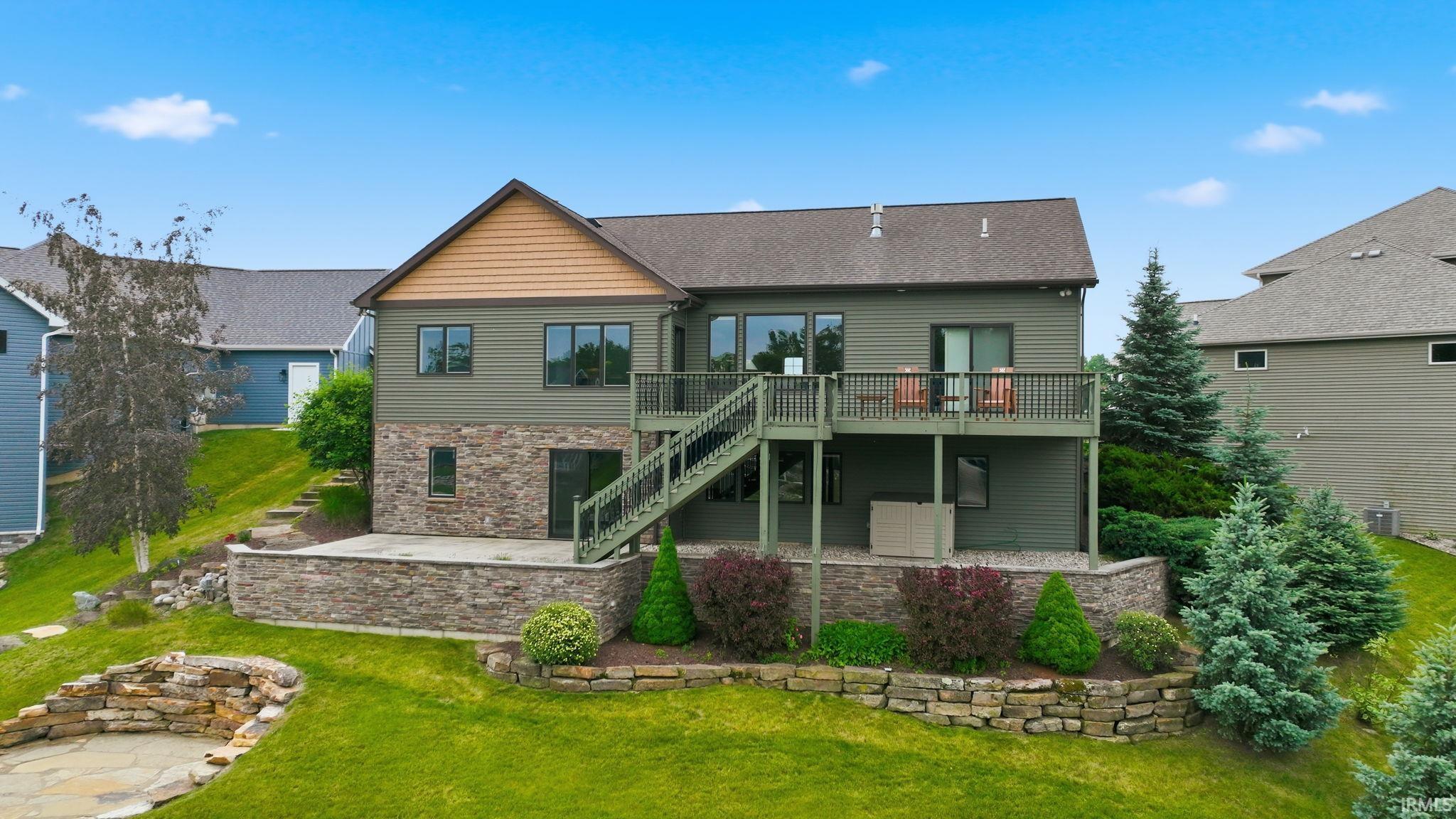 Image 3: Rear exterior featuring a multi-level deck, lower patio, stone retaining walls, mature landscaping, and an upper-level balcony, Back Of Structure Image 3: Rear exterior featuring a multi-level deck, lower patio, stone retaining walls, mature landscaping, and an upper-level balcony, Back Of Structure