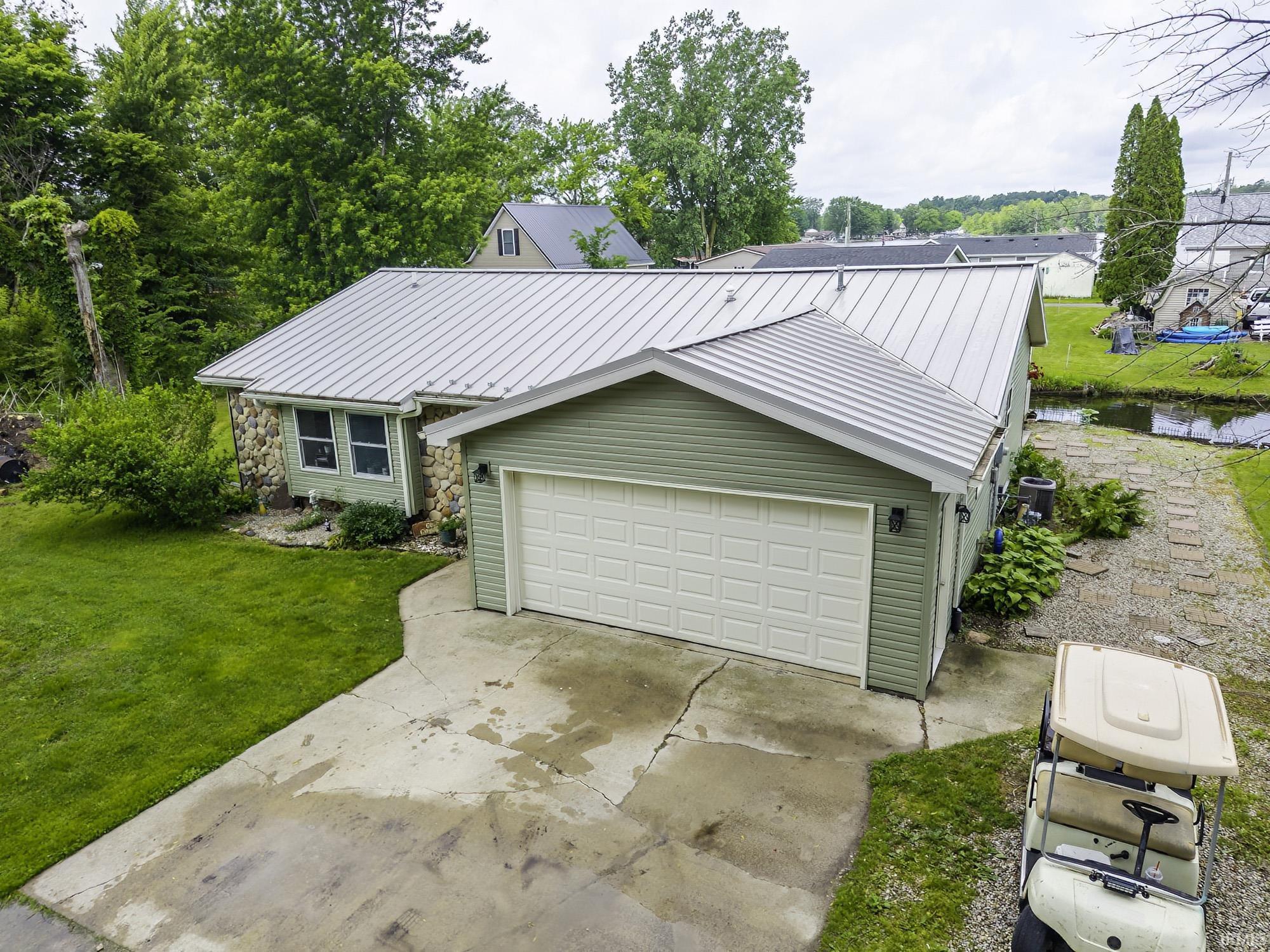 Image 1: Single-story residence featuring a two-car garage, light green siding, stone accents, and a metal roof, Front Of Structure