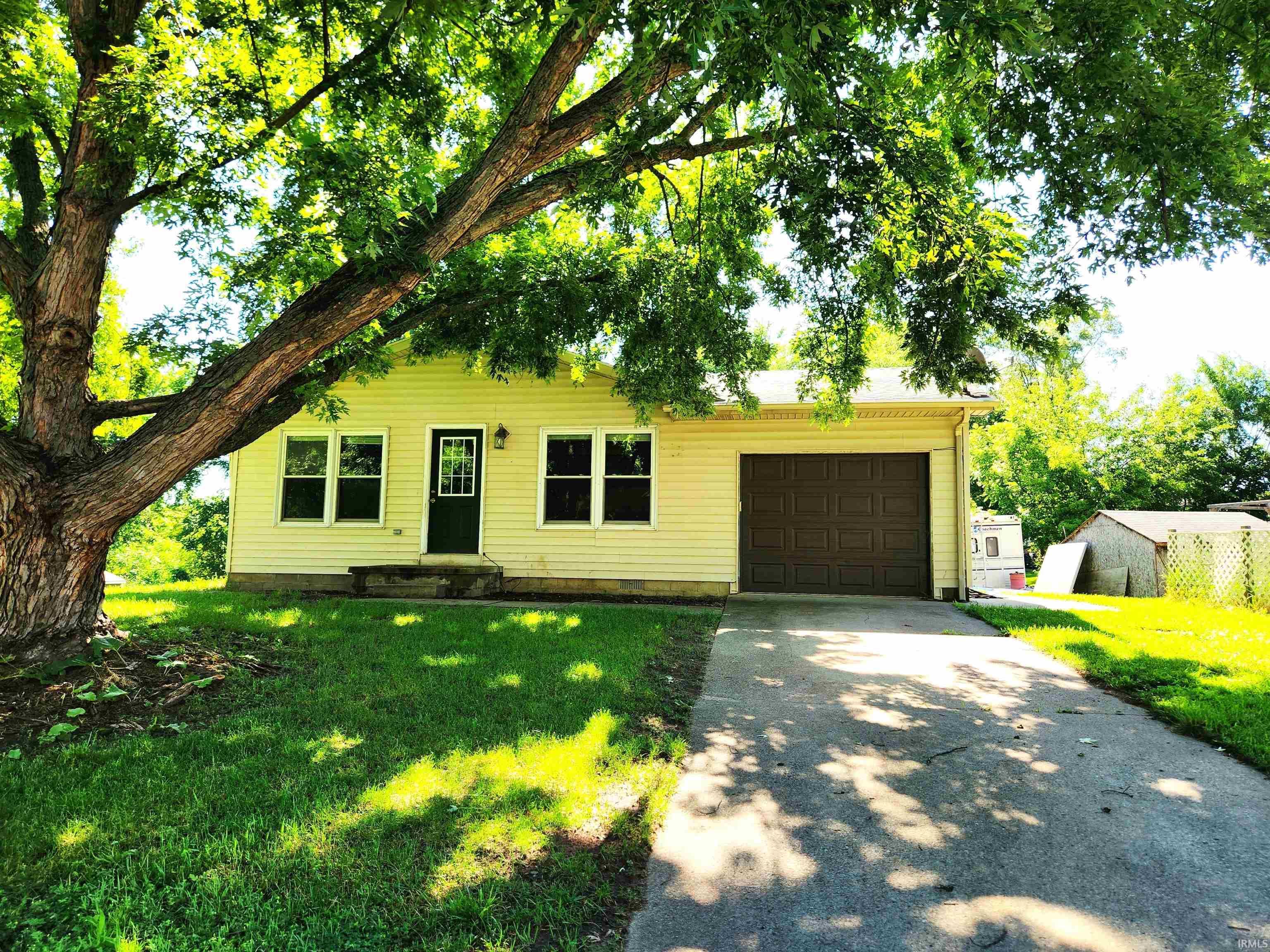 Image 2: Single-story home featuring light-colored siding, a dark paneled front door, and a single-car garage with a brown sectional door, Front Of Structure
