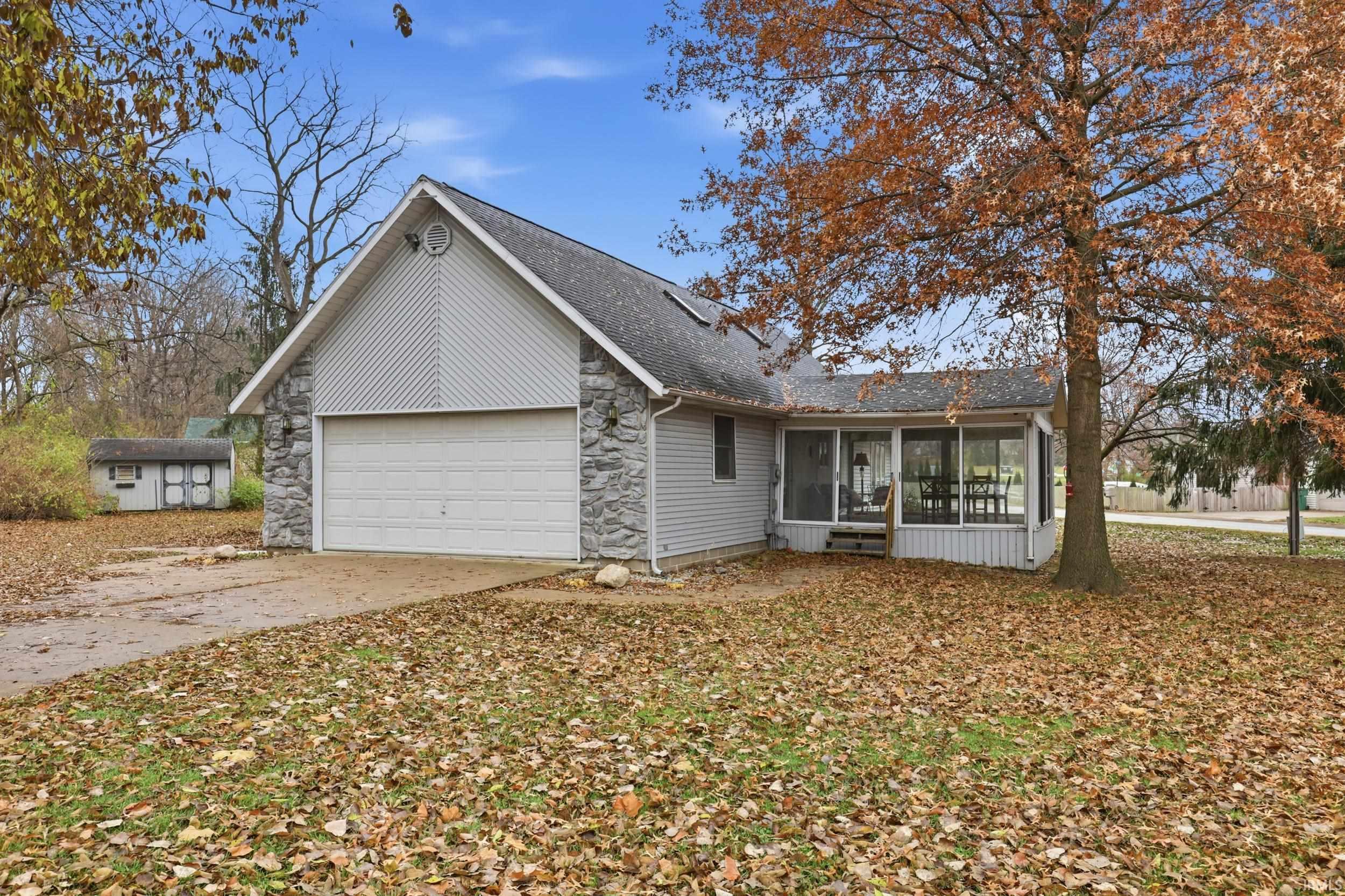 Image 2: View of front of house featuring a sunroom, driveway, stone siding, a garage, and roof with shingles, Front Of Structure Image 2: View of front of house featuring a sunroom, driveway, stone siding, a garage, and roof with shingles, Front Of Structure