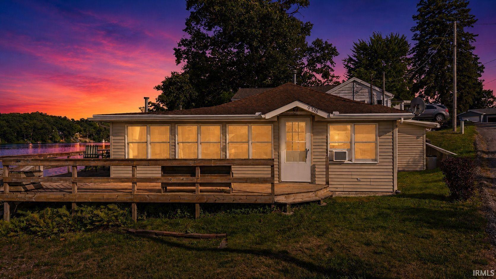 Image 0: Waterfront property featuring a spacious deck overlooking the lake, light-colored siding, and a prominent front door, Back Of Structure Image 0: Waterfront property featuring a spacious deck overlooking the lake, light-colored siding, and a prominent front door, Back Of Structure