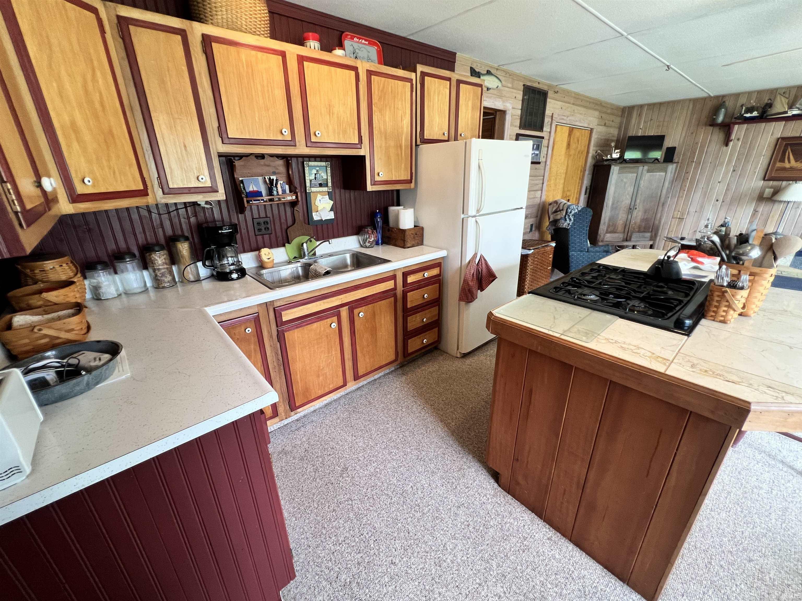 Image 1: Kitchen featuring wood-finish cabinetry with red trim, a double basin stainless steel sink, and light-toned countertops, Kitchen