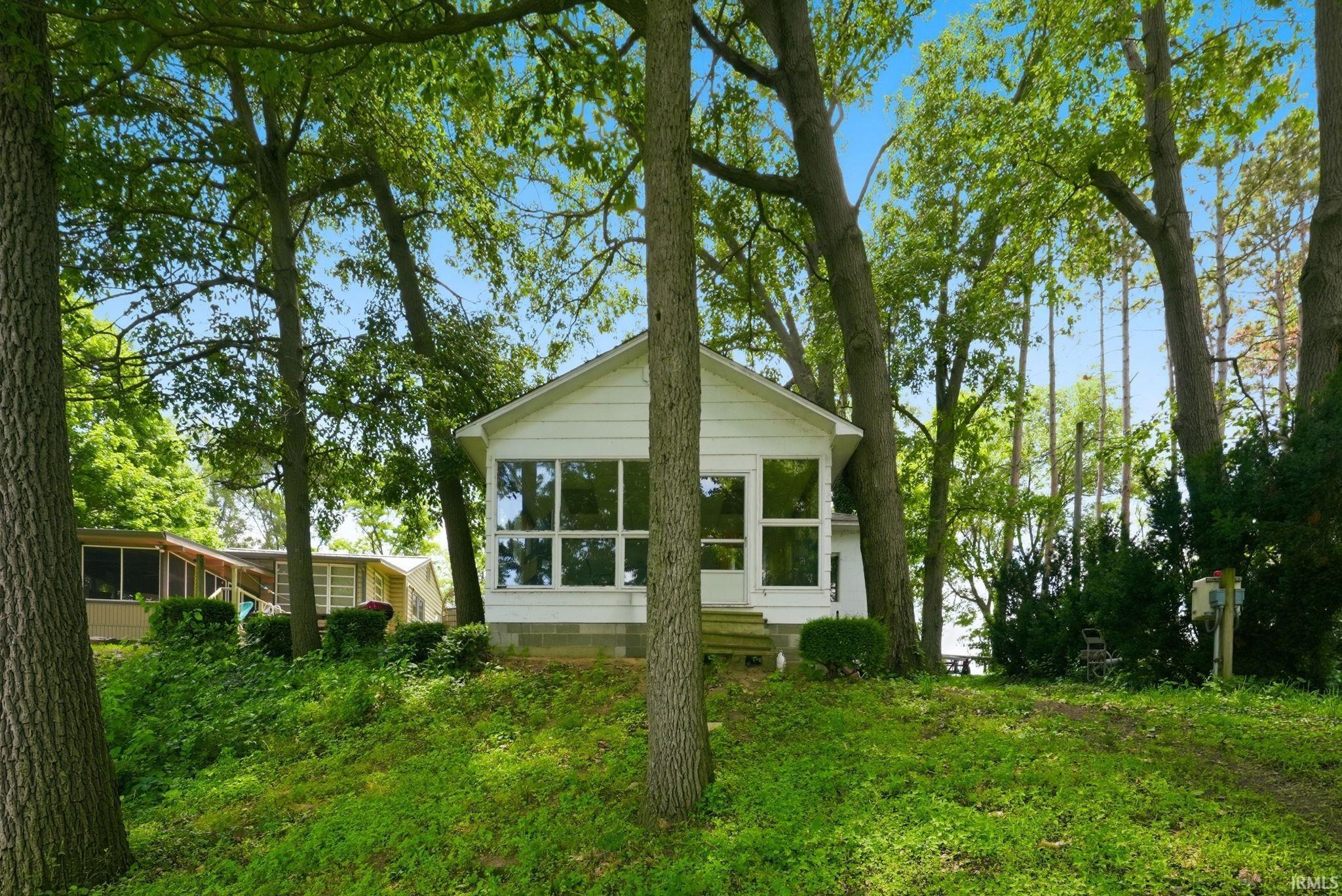Image 2: Wooded property featuring a white cottage with a covered front entrance and multiple windows, Front Of Structure Image 2: Wooded property featuring a white cottage with a covered front entrance and multiple windows, Front Of Structure