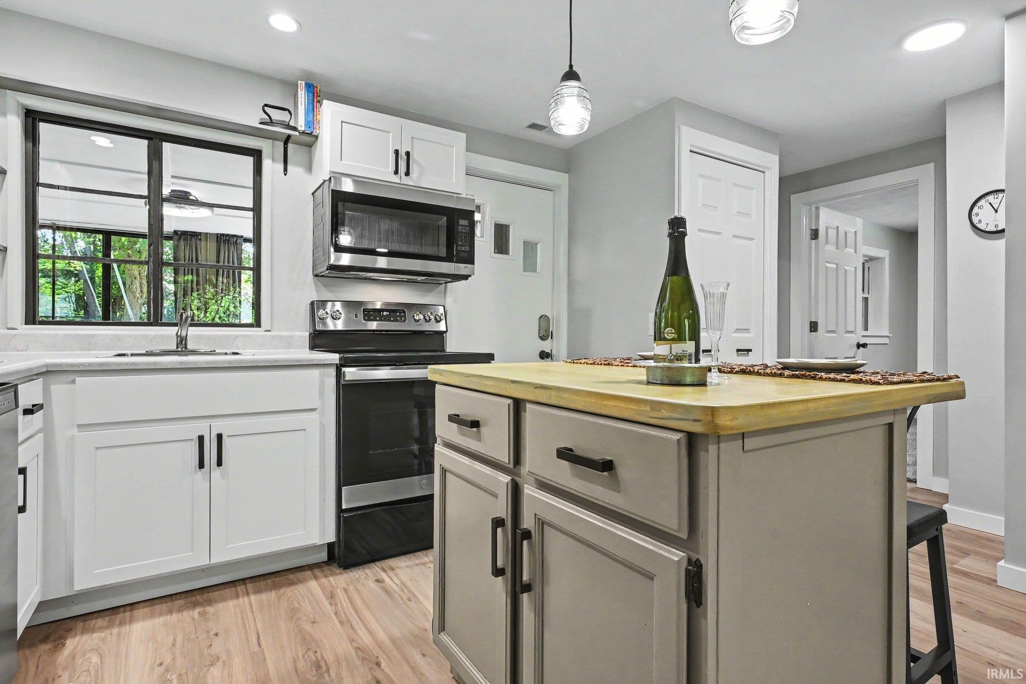 Image 3: Modern kitchen featuring a central island with a light wood-finish countertop, white cabinetry with black hardware, stainless steel appliances, and wood-finish flooring, Kitchen