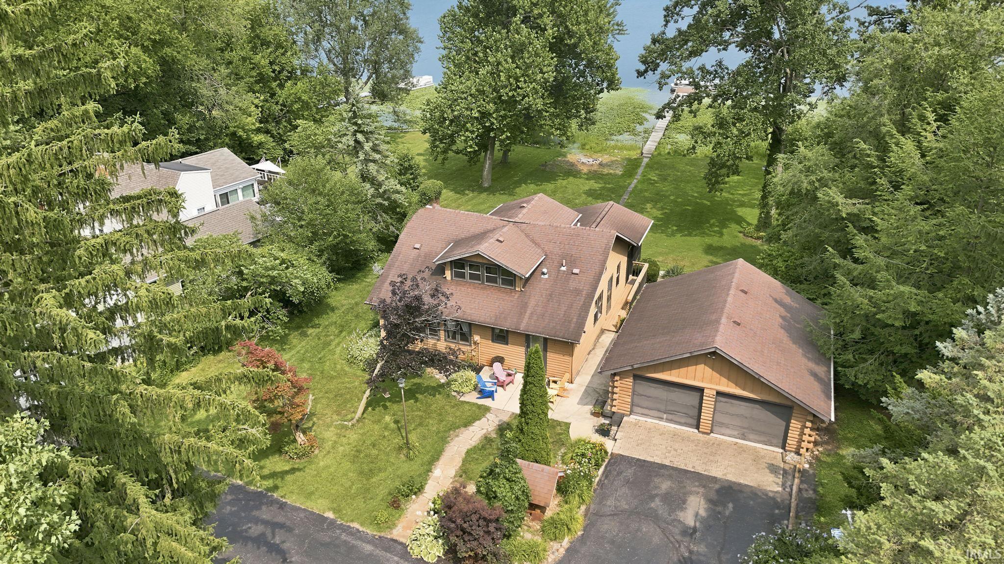 Image 1: Waterfront property featuring a private dock, mature trees, an attached garage with a paved driveway, and a sloped lawn, Aerial View Image 1: Waterfront property featuring a private dock, mature trees, an attached garage with a paved driveway, and a sloped lawn, Aerial View