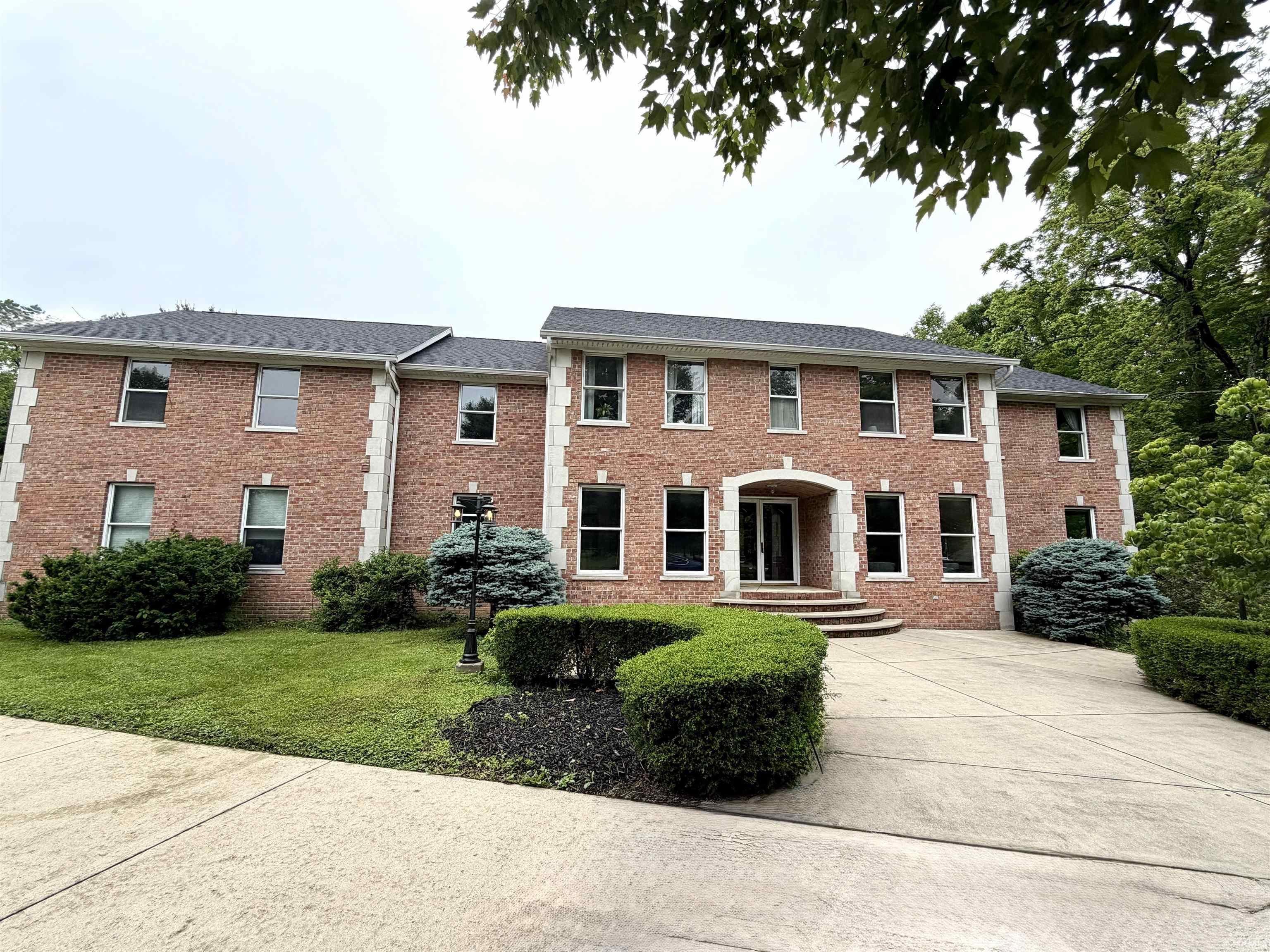 Image 0: Brick exterior featuring white window trim, a multi-pane front door, and a concrete driveway, Front Of Structure Image 0: Brick exterior featuring white window trim, a multi-pane front door, and a concrete driveway, Front Of Structure