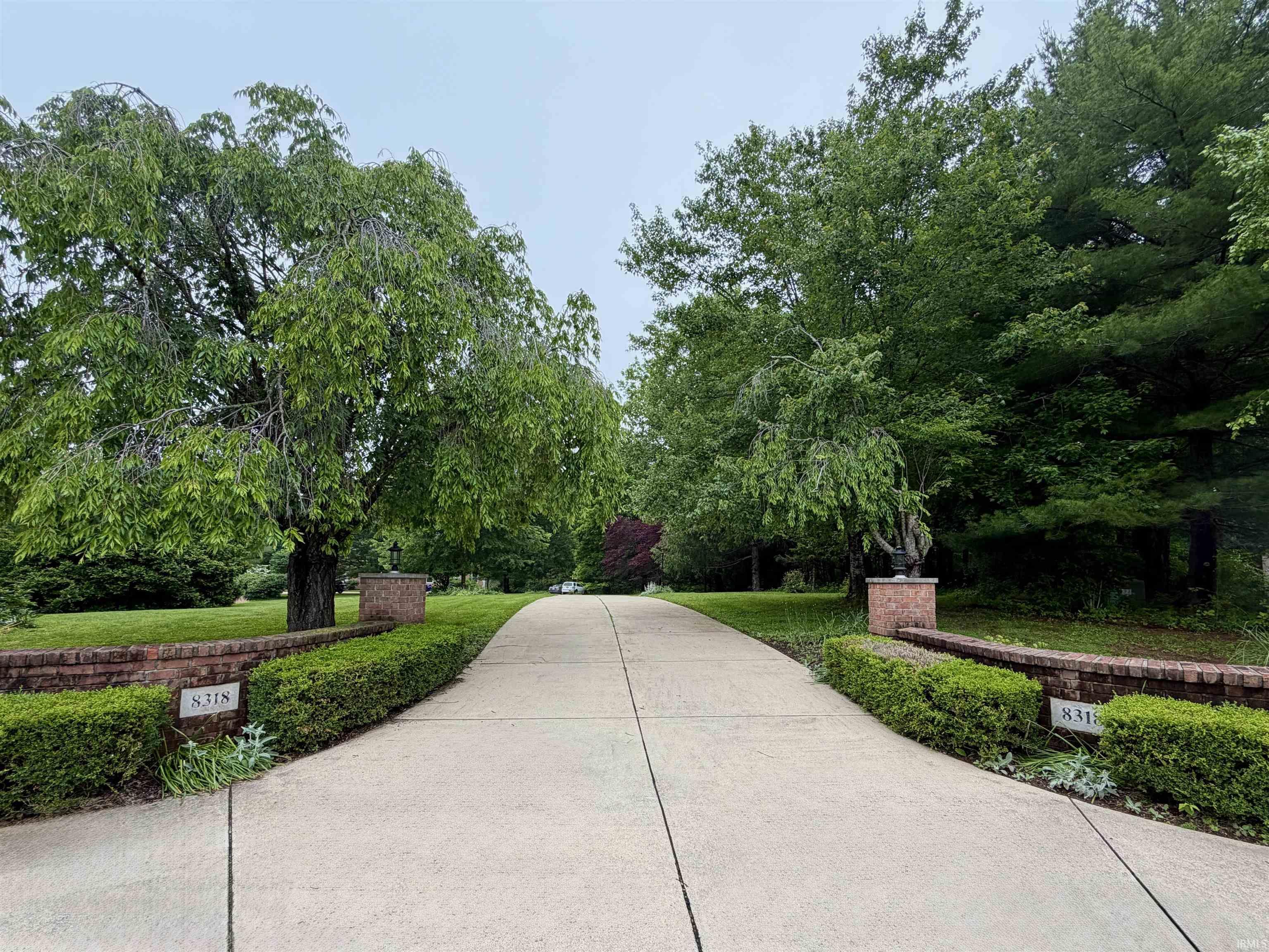 Image 2: Concrete driveway framed by mature trees, brick pillars, manicured hedges, and lush green lawns, Private Driveway entrance Image 2: Concrete driveway framed by mature trees, brick pillars, manicured hedges, and lush green lawns, Private Driveway entrance