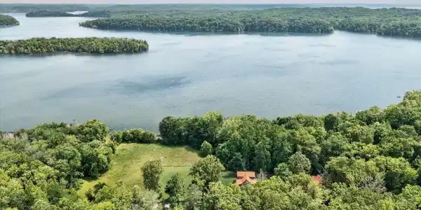 Image 2: Expansive waterfront property featuring a lake, surrounding mature woodlands, and a partially cleared land parcel, Aerial View Image 2: Expansive waterfront property featuring a lake, surrounding mature woodlands, and a partially cleared land parcel, Aerial View