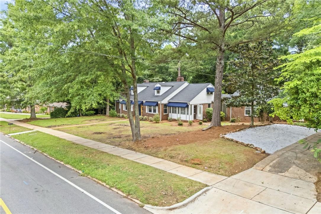 Image 2: Mature trees frame a charming home with awnings, a