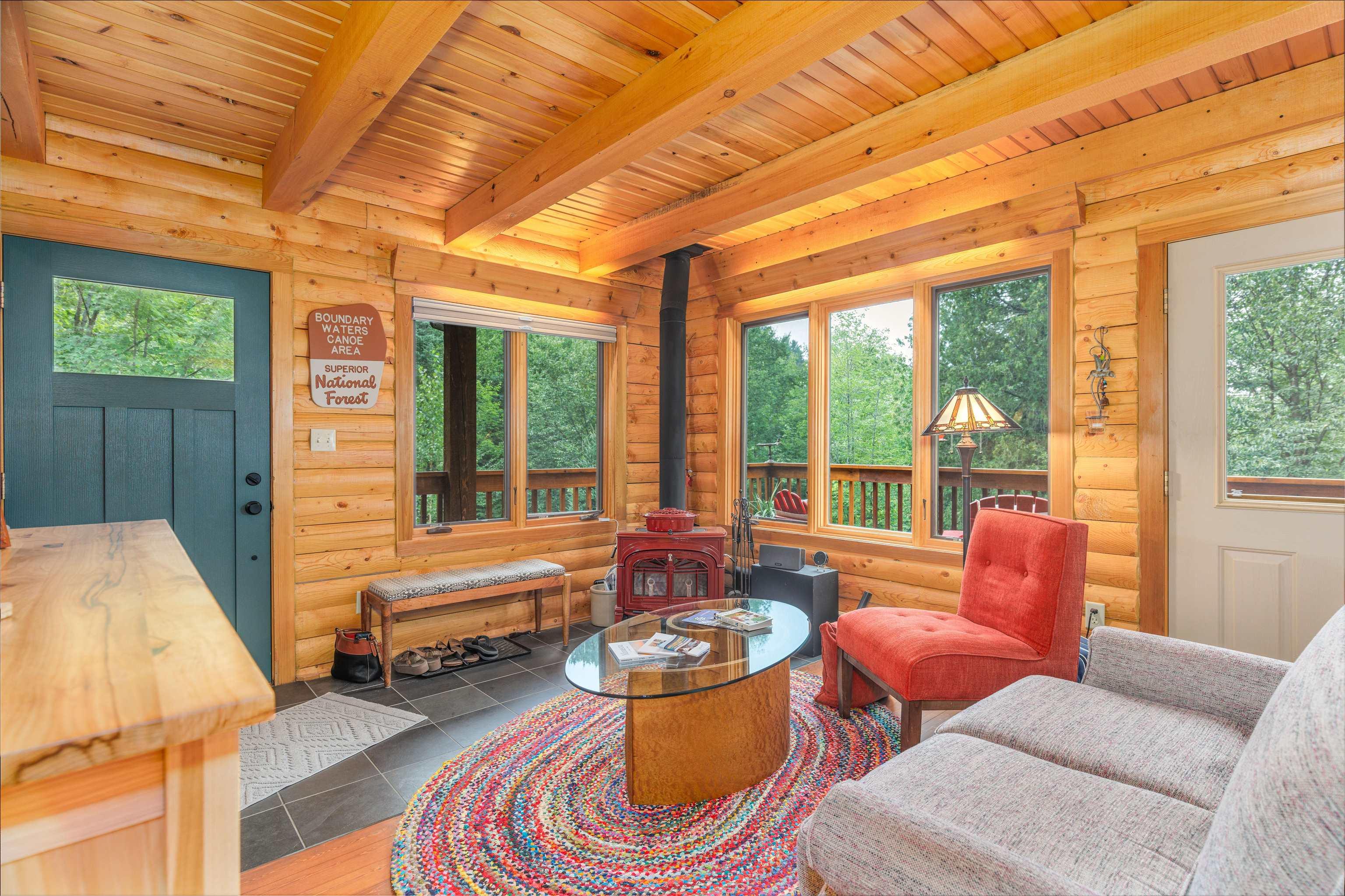 Image 2: Living area featuring a wood stove, a wooden ceiling with exposed beams, rustic walls, plenty of natural light, and tile patterned floors, Living Room