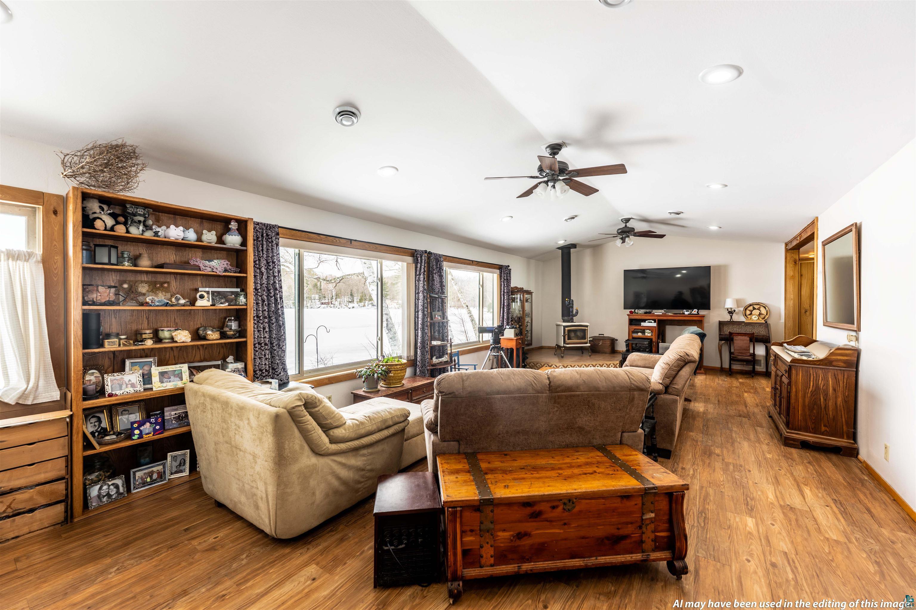 Image 3: Living area with wood-type flooring, a wood stove, vaulted ceiling, and a ceiling fan, Living Room