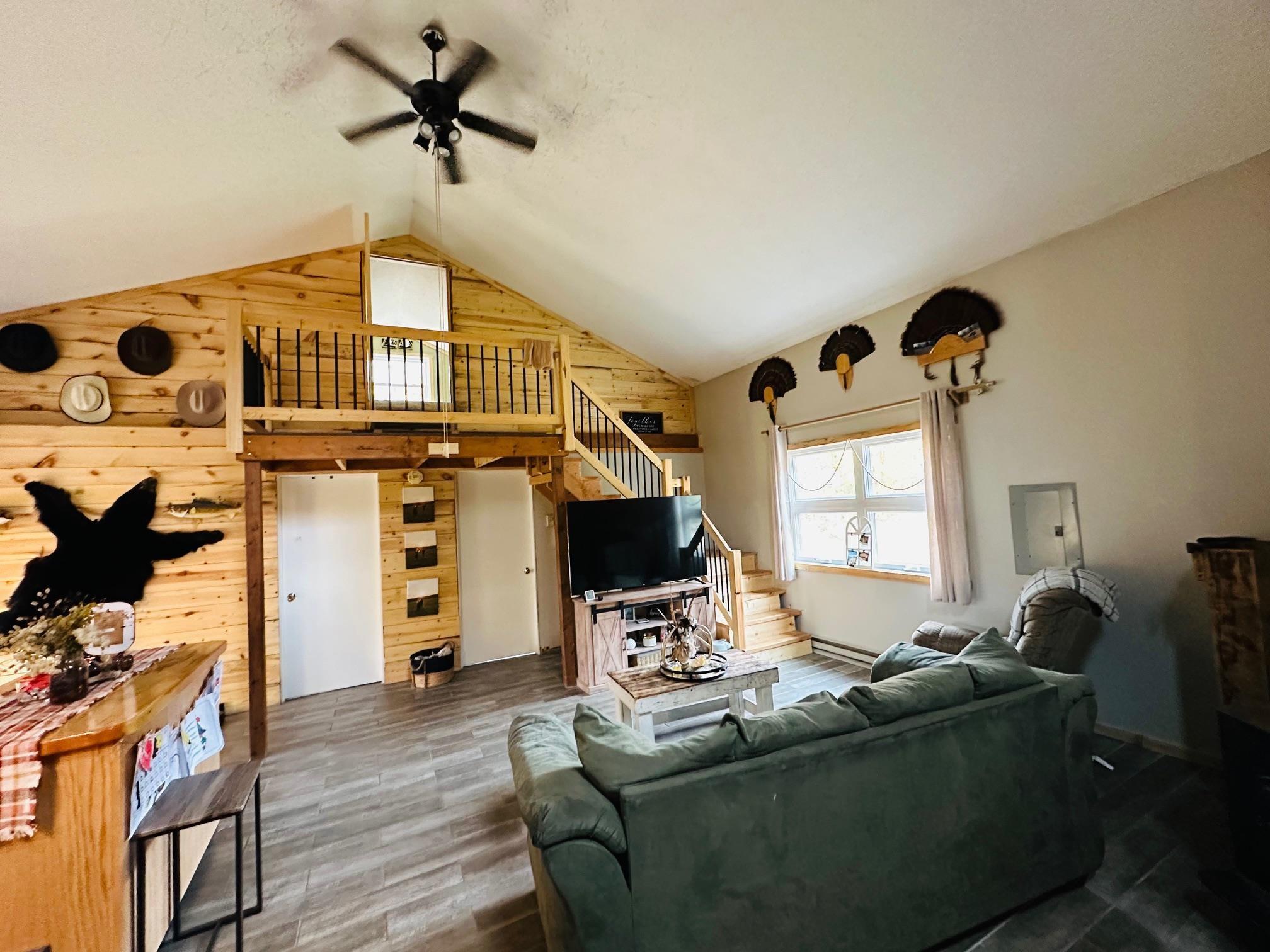 Image 2: Living room with wood walls, stairs, ceiling fan, wood finished floors, and electric panel, Living Room