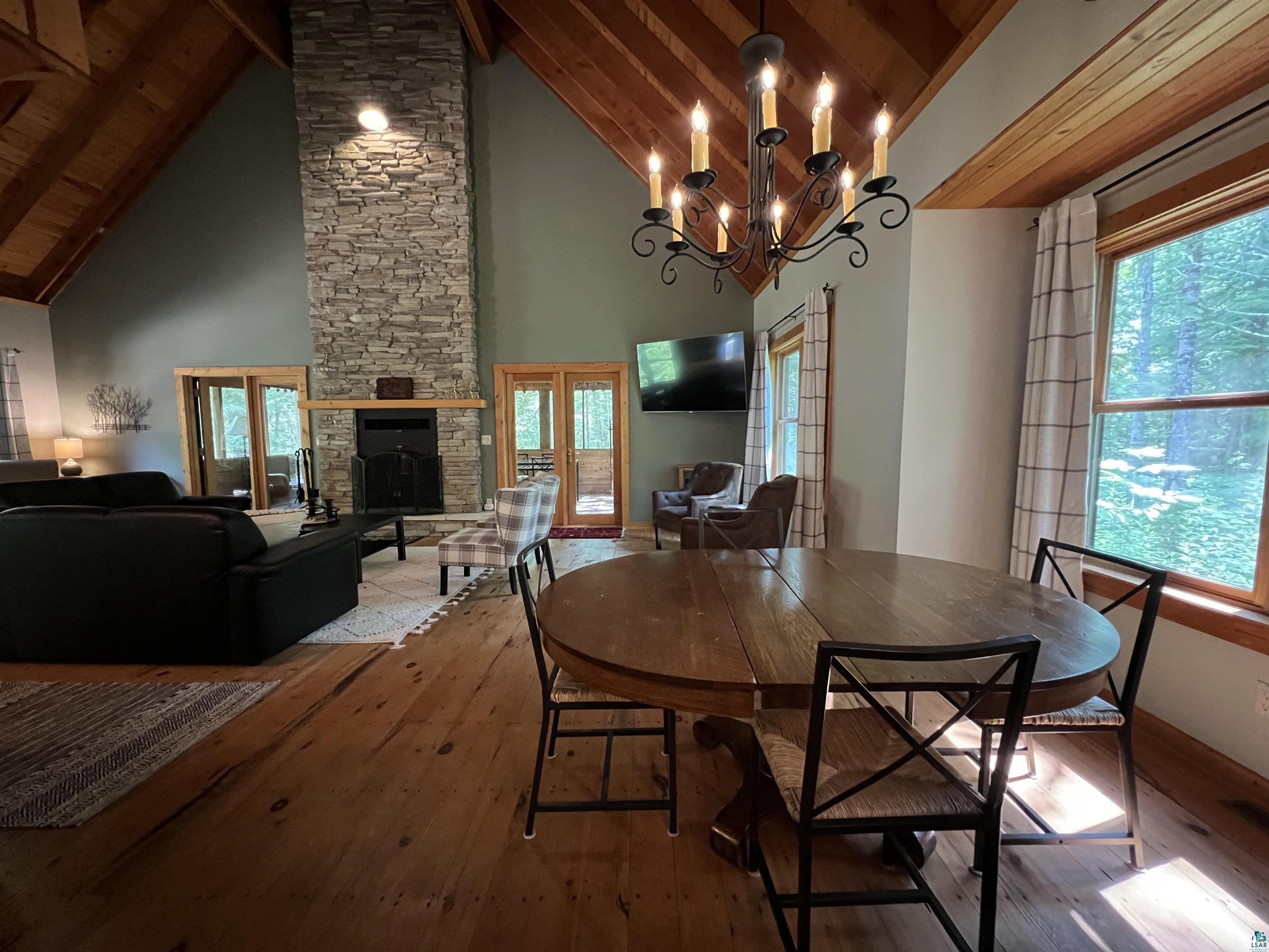 Image 1: Dining room featuring wood-type flooring, a stone fireplace, hanging lights, and a high wood beamed ceiling, Dining Area