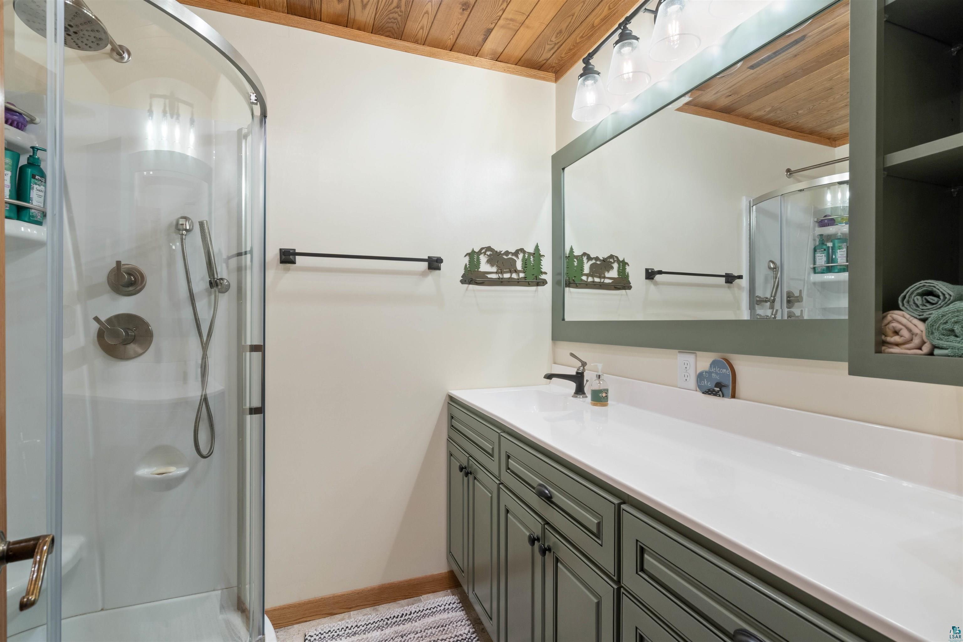 Image 3: Bathroom featuring a wood-finish ceiling, enclosed shower with brushed nickel fixtures, custom vanity with ample storage, integrated sink, and an expansive wall-mounted mirror, Bathroom