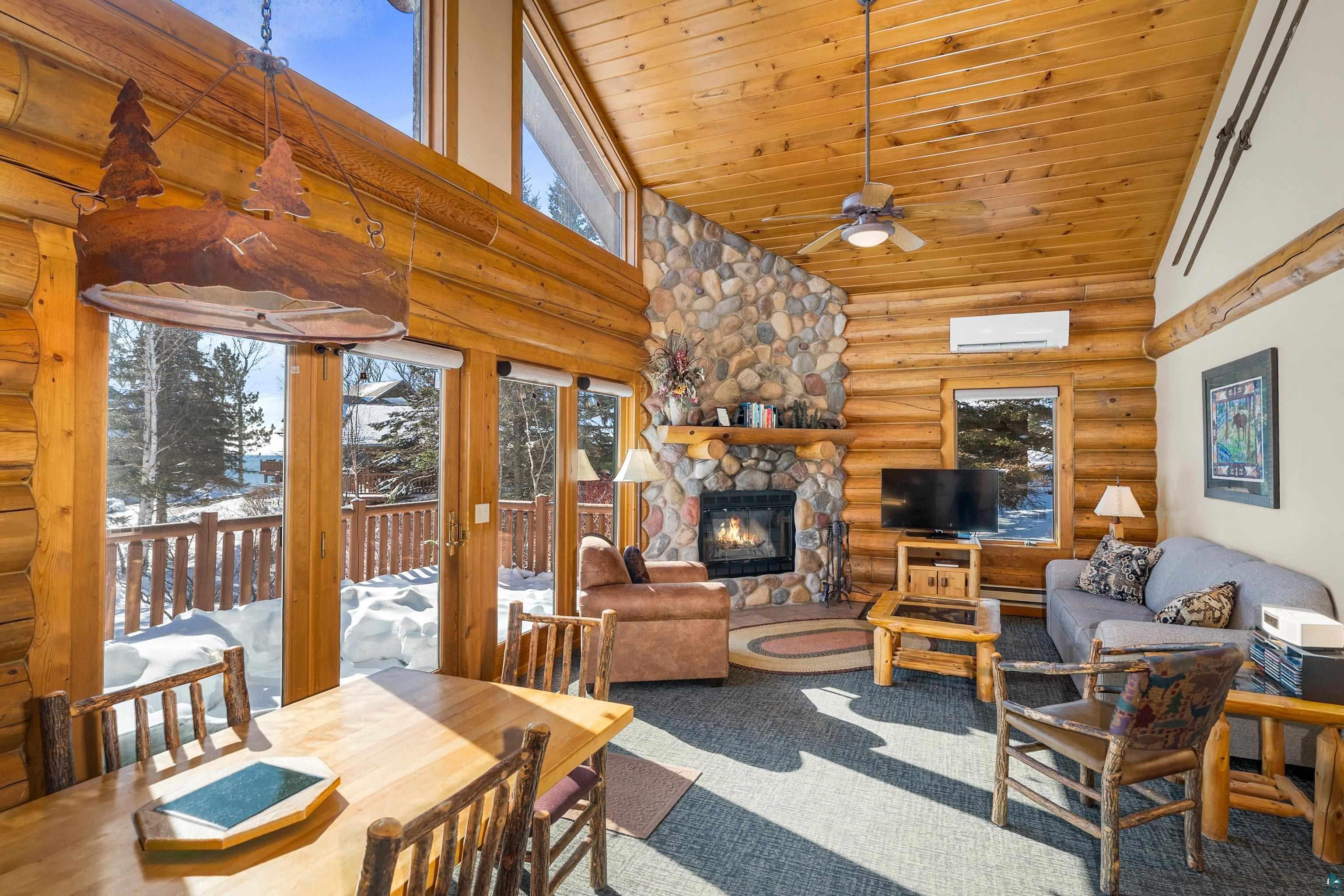 Image 1: Carpeted living area with log walls, a stone fireplace, a vaulted wooden ceiling, a ceiling fan, and baseboard heating, Living Room