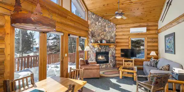 Image 1: Carpeted living area with log walls, a stone fireplace, a vaulted wooden ceiling, a ceiling fan, and baseboard heating, Living Room
