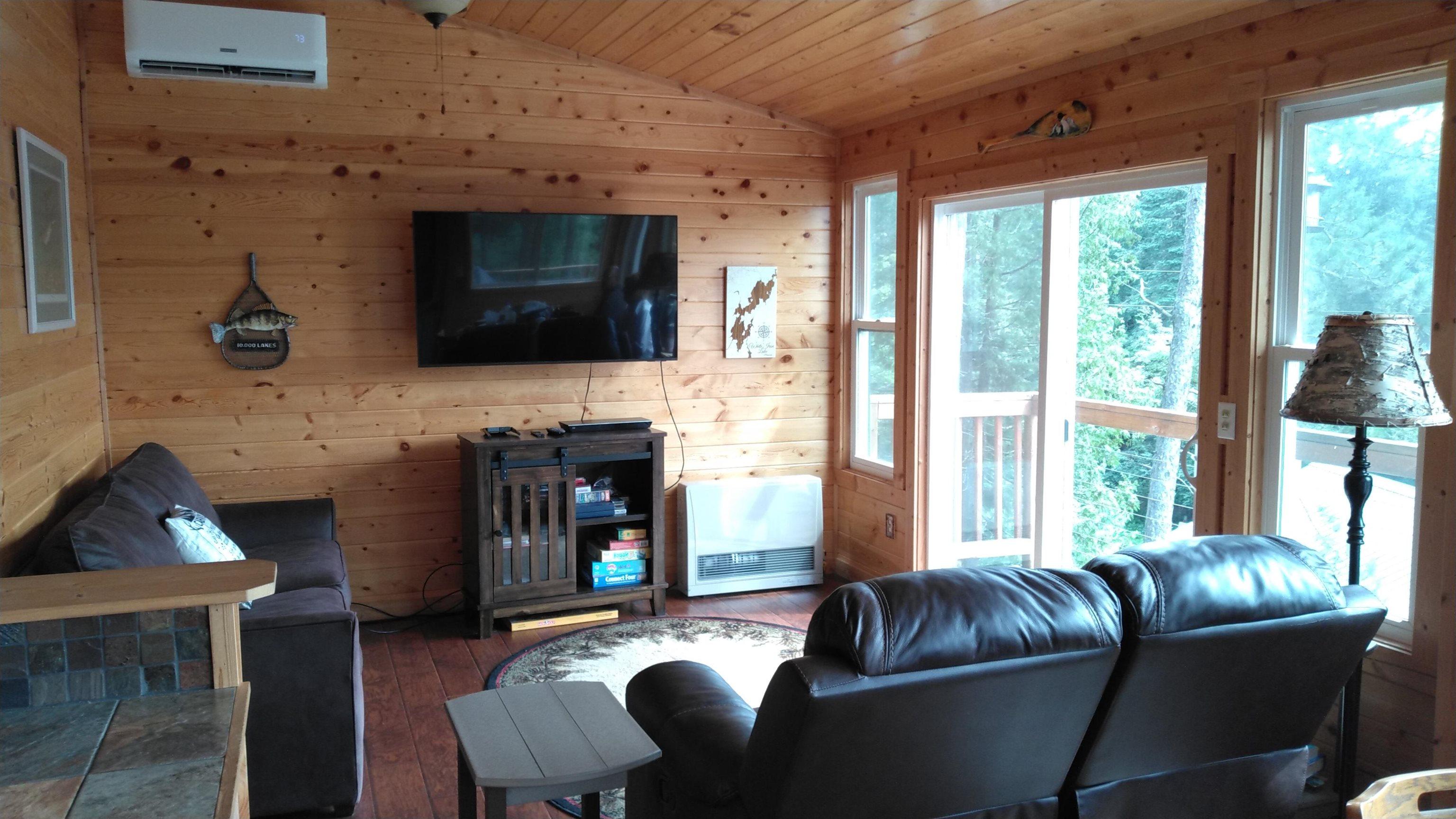 Image 2: Living area with wooden walls, vaulted ceiling, hardwood / wood-style floors, wood ceiling, and a wall unit AC, Living Room