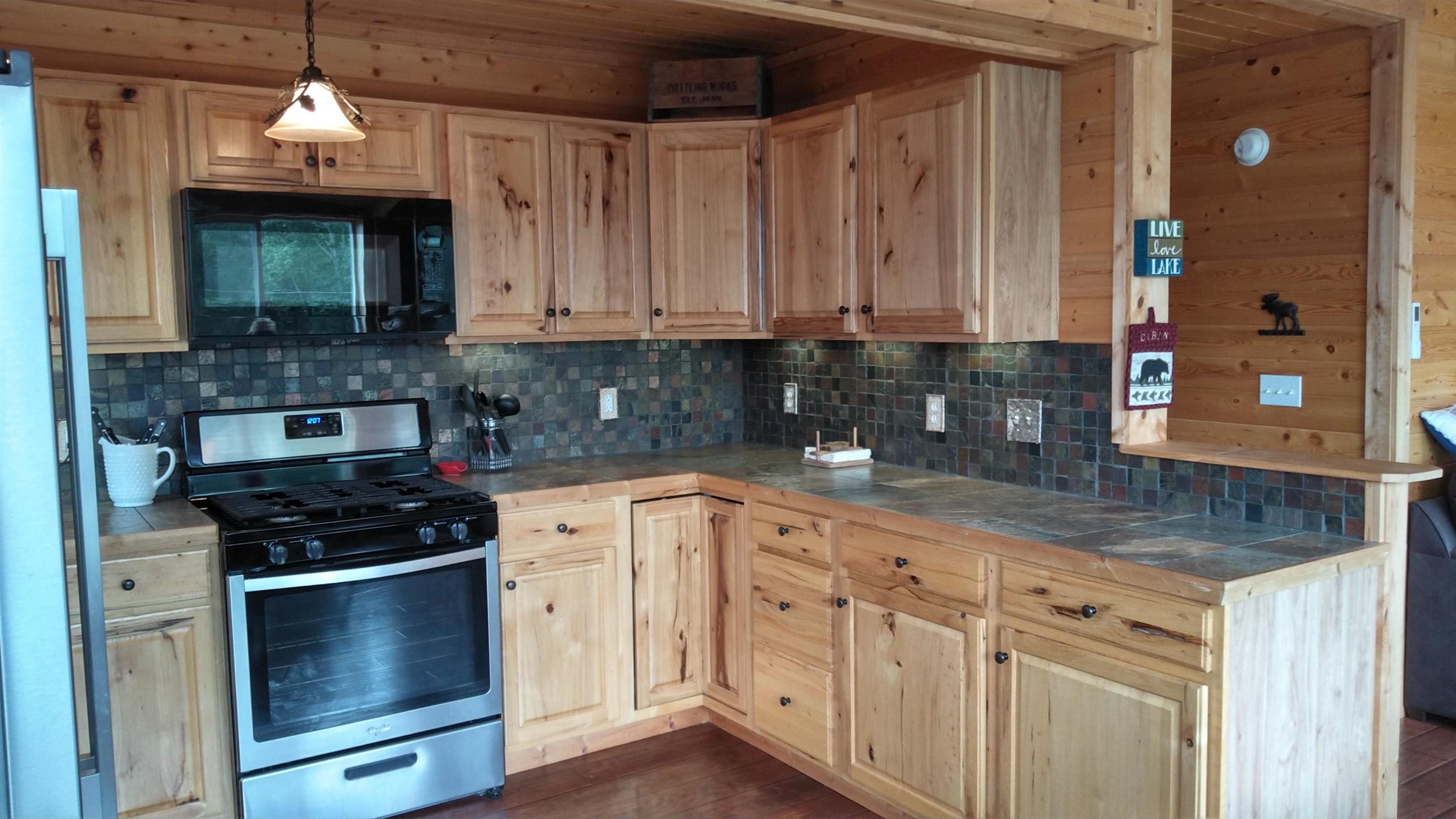 Image 3: Kitchen featuring stainless steel range with gas cooktop, black microwave, tile counters, backsplash, and light brown cabinetry, Kitchen