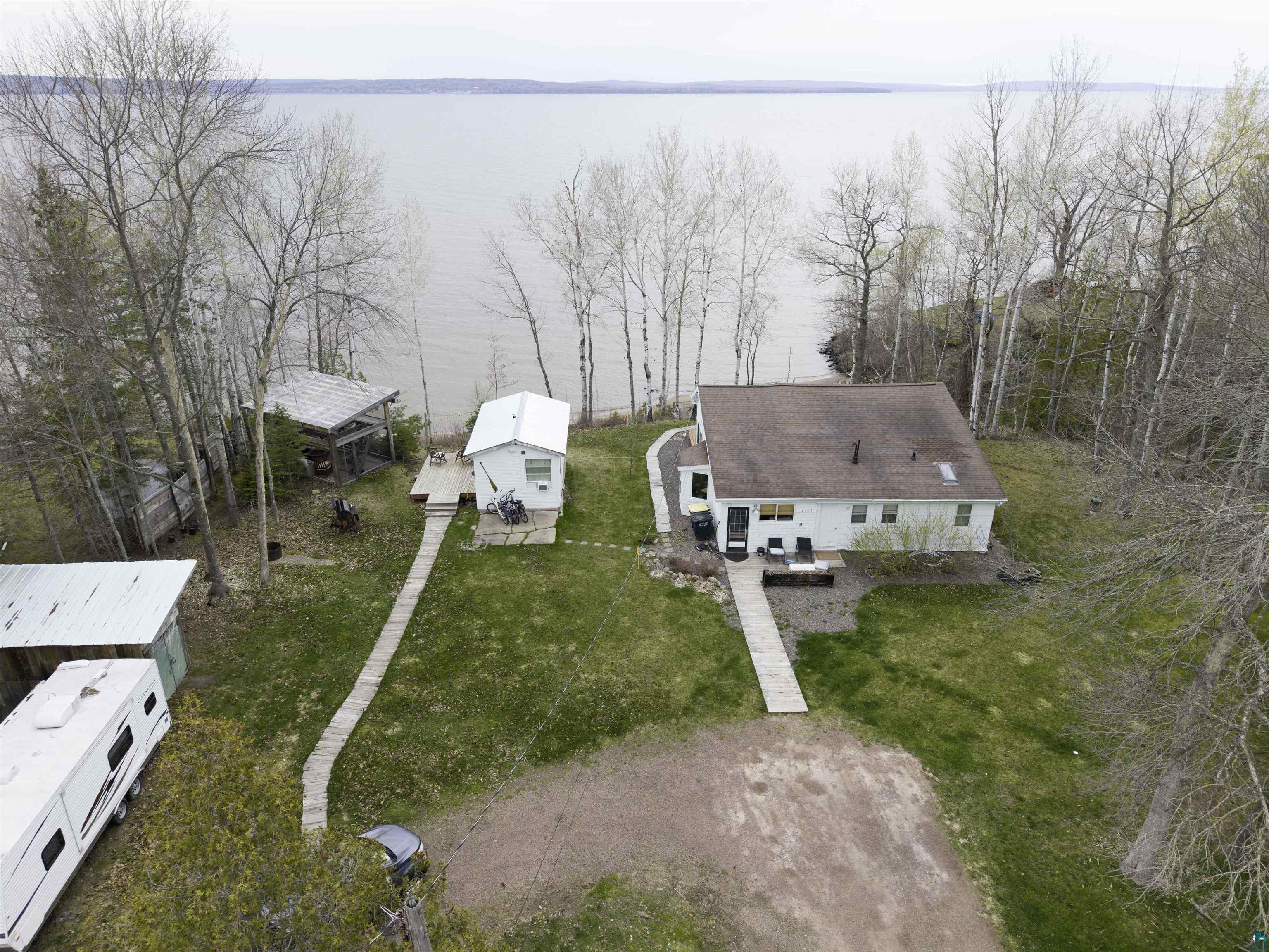 Image 1: Waterfront property featuring a primary residence, a detached secondary structure with a deck, a separate outbuilding, and mature trees, Aerial View