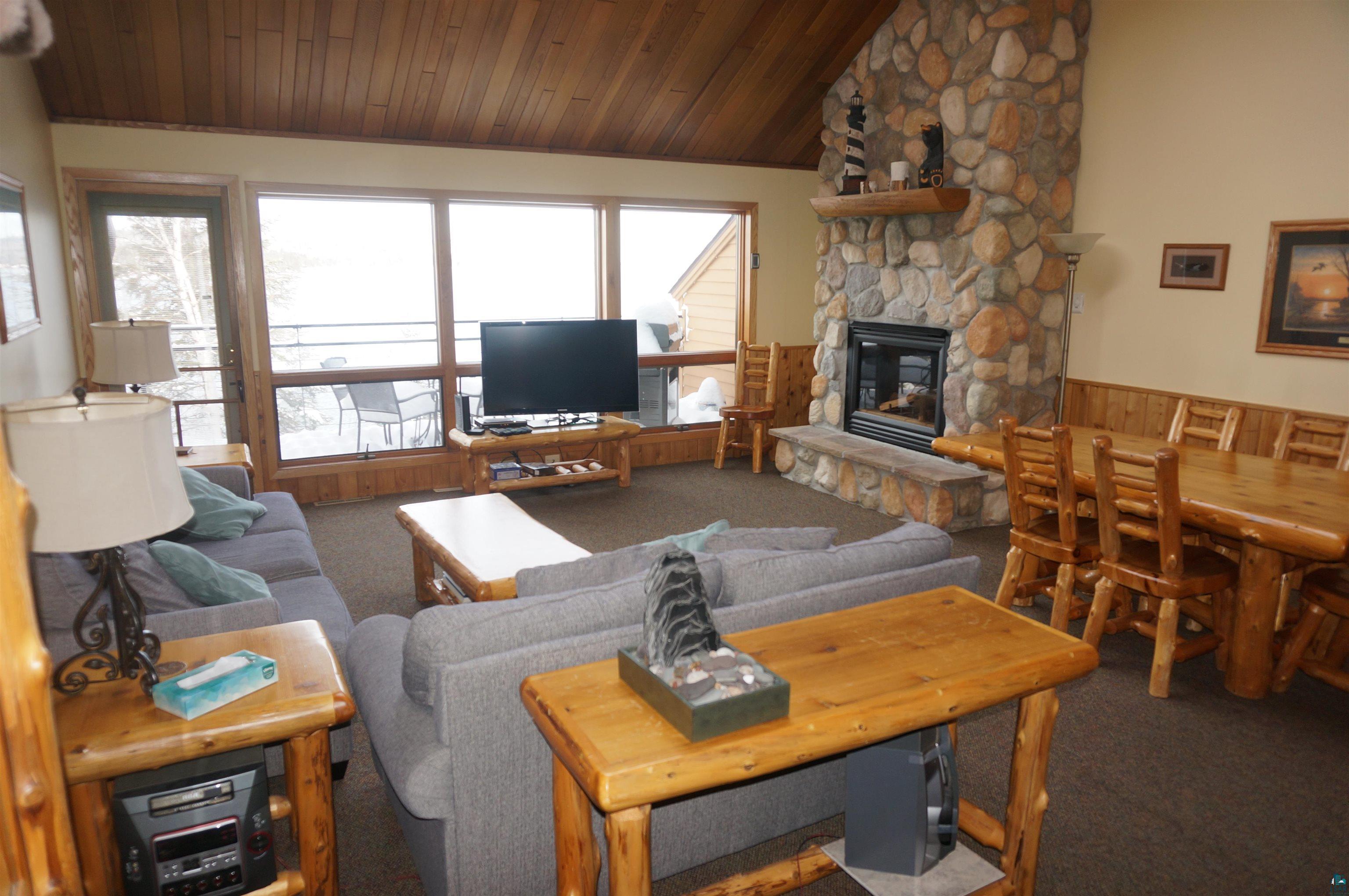 Image 1: Carpeted living area featuring a stone fireplace, lofted ceiling, wooden ceiling, and a wainscoted wall, Living Room