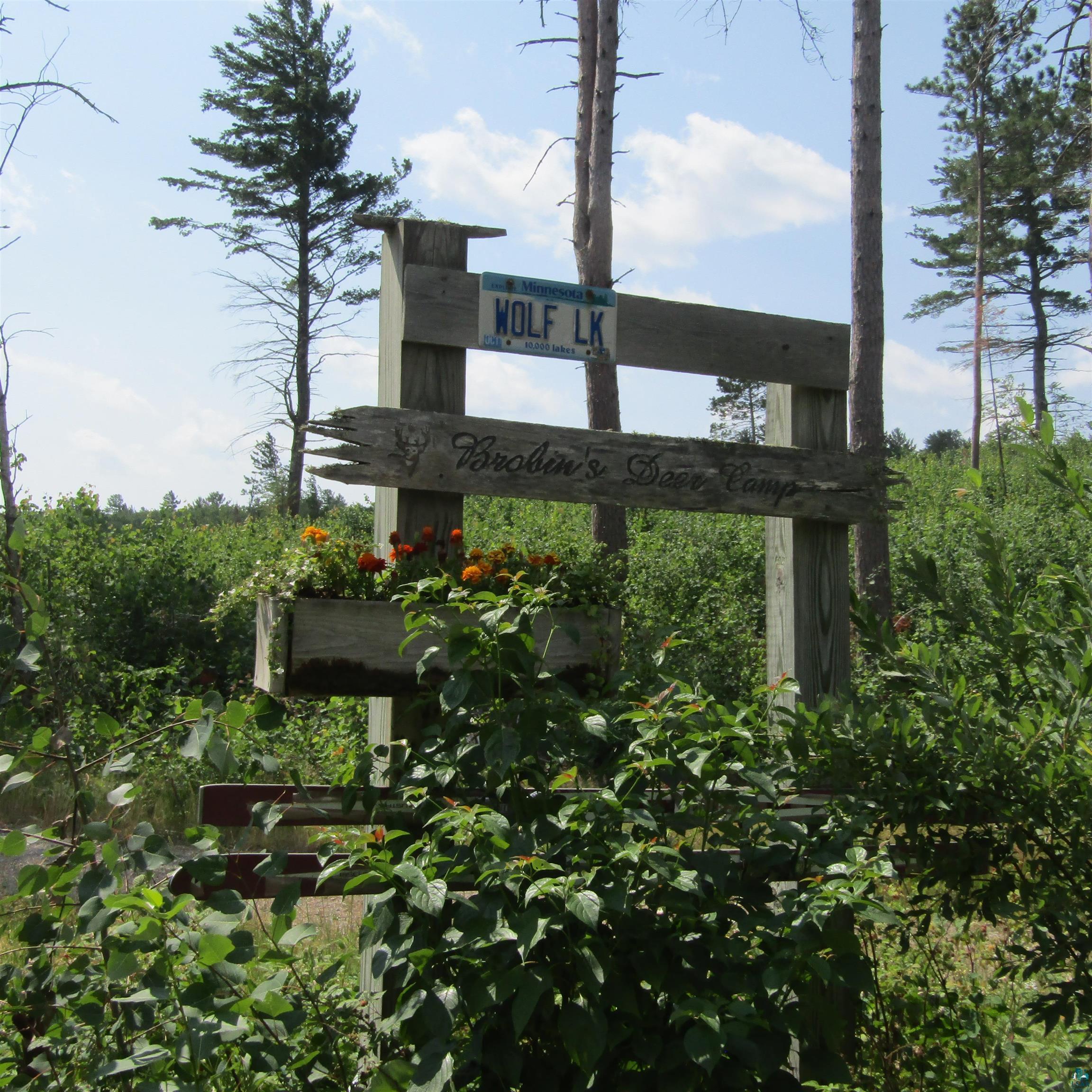 Image 0: Rustic wooden sign structure featuring a planter box with blooming orange and white flowers, Brobin's Deer Camp