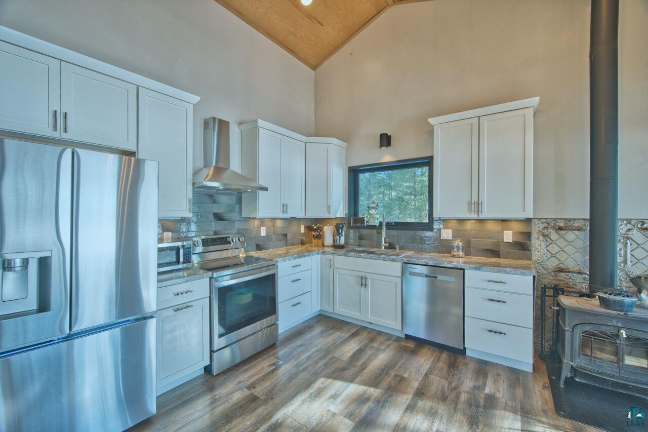 Image 3: Kitchen with a wood stove, stainless steel appliances, dark wood-type flooring, white cabinets, and vaulted ceiling, Kitchen