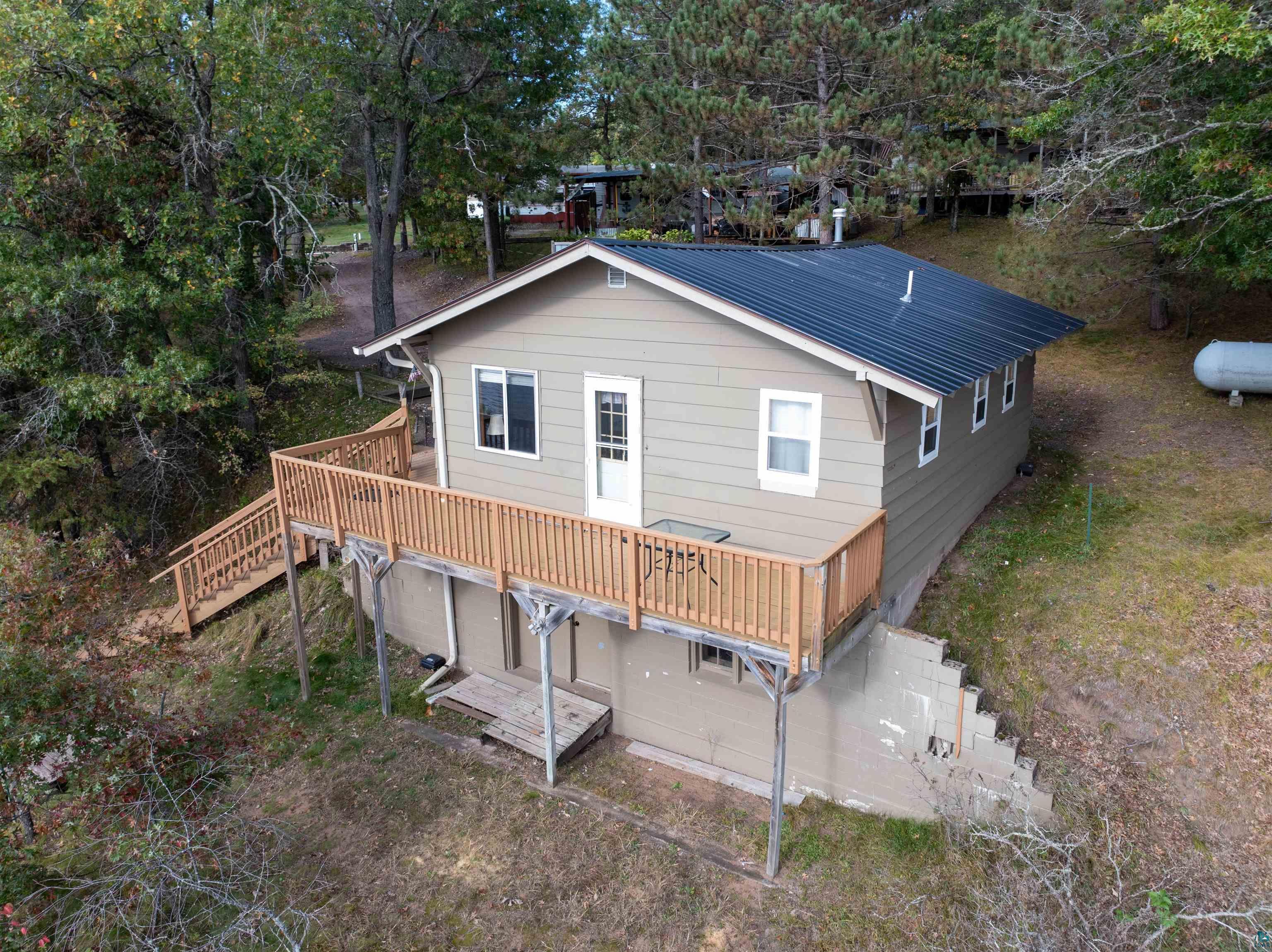 Image 1: Rear view of property with a deck, a metal roof, and view of wooded area, Back Of Structure
