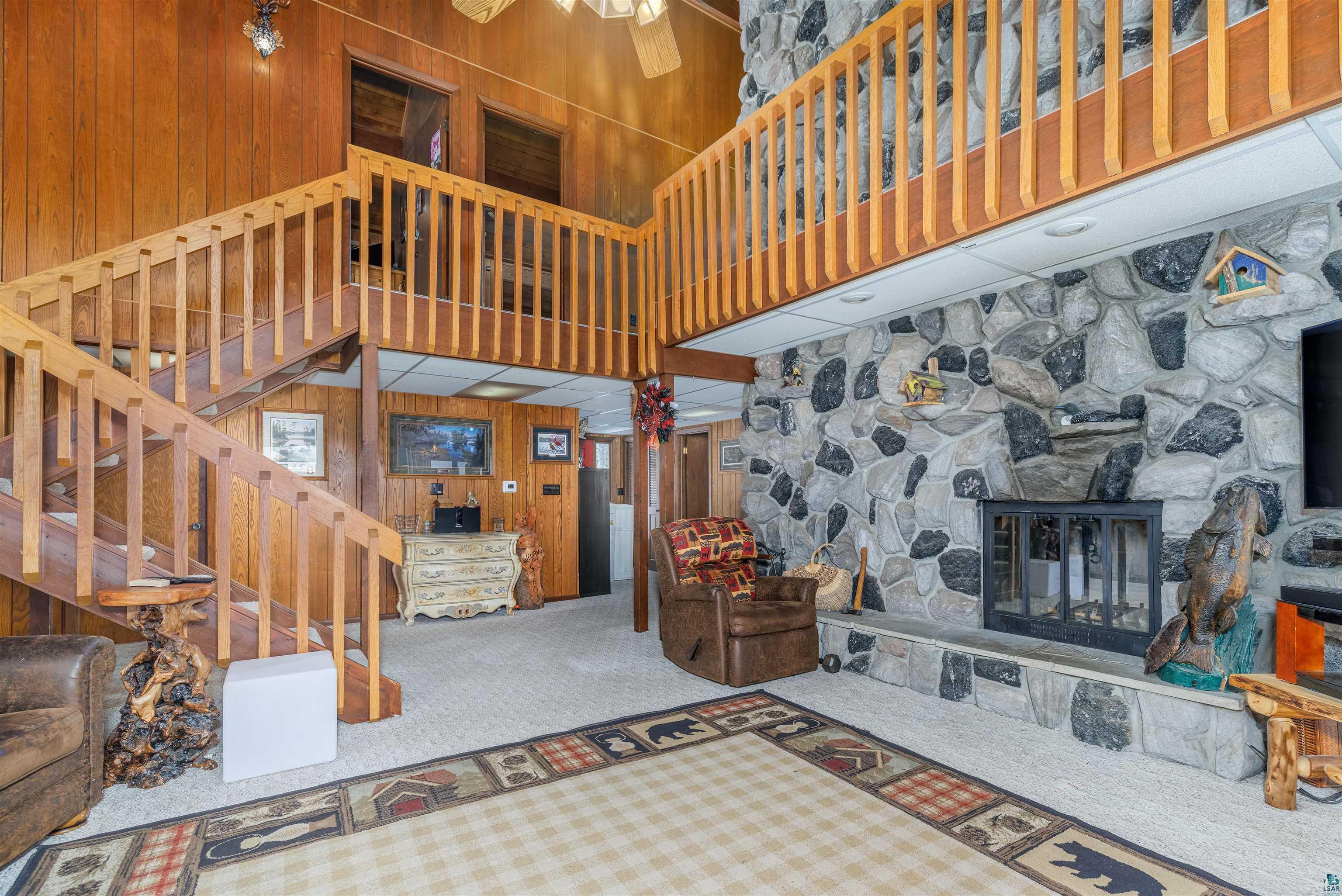 Image 3: Carpeted living room with wood walls, a high ceiling, ceiling fan, and a fireplace, Living Room