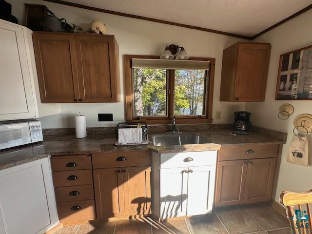 Image 3: Kitchen with a textured ceiling, crown molding, dark stone counters, white microwave, and brown cabinetry, Kitchen
